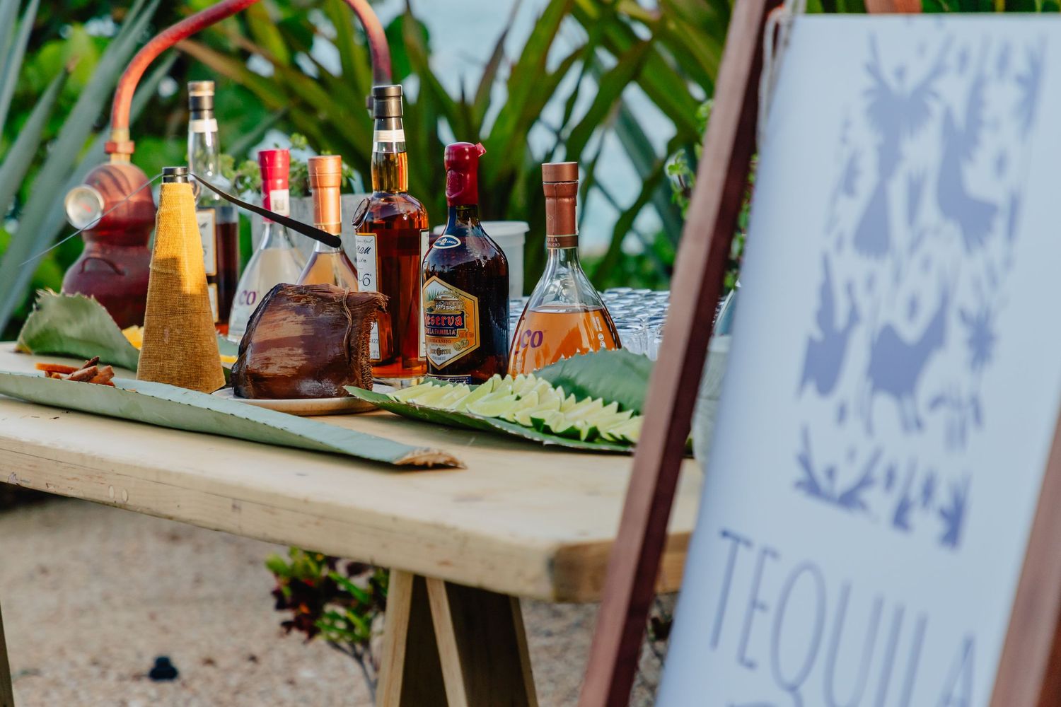 Rustic wooden bar setup with tequila bottles and cocktail signage at an outdoor event.