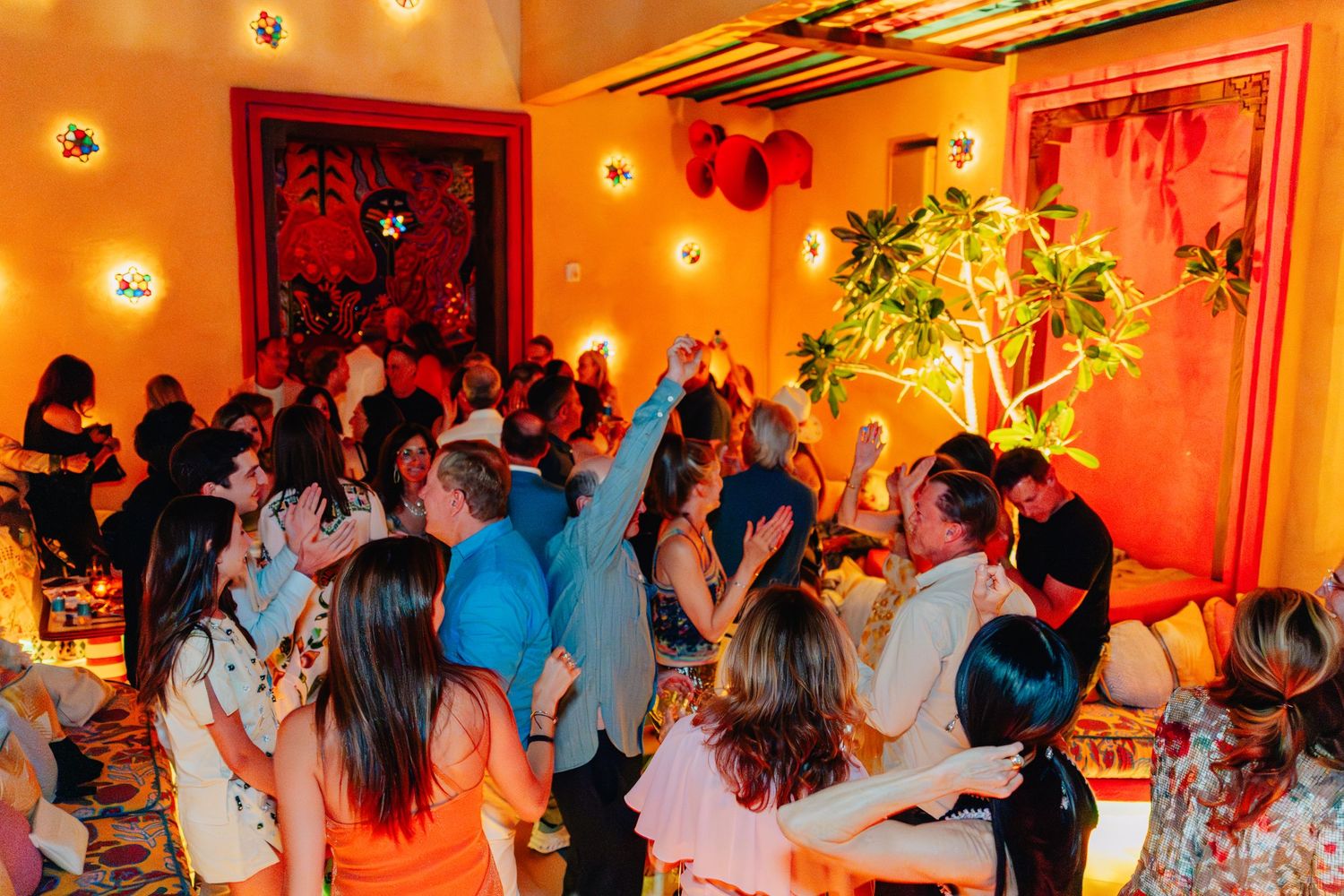 Wedding reception dance party with guests dancing under warm orange and red lighting on a crowded dance floor.