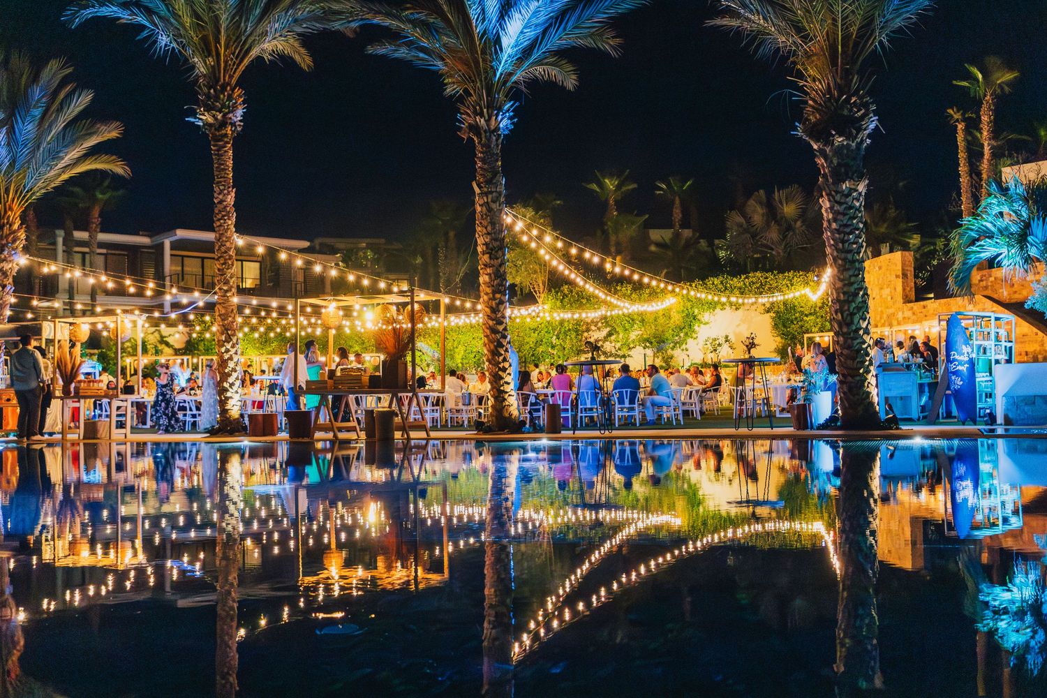 Palm trees and string lights reflected in pool water at night creating magical ambiance.