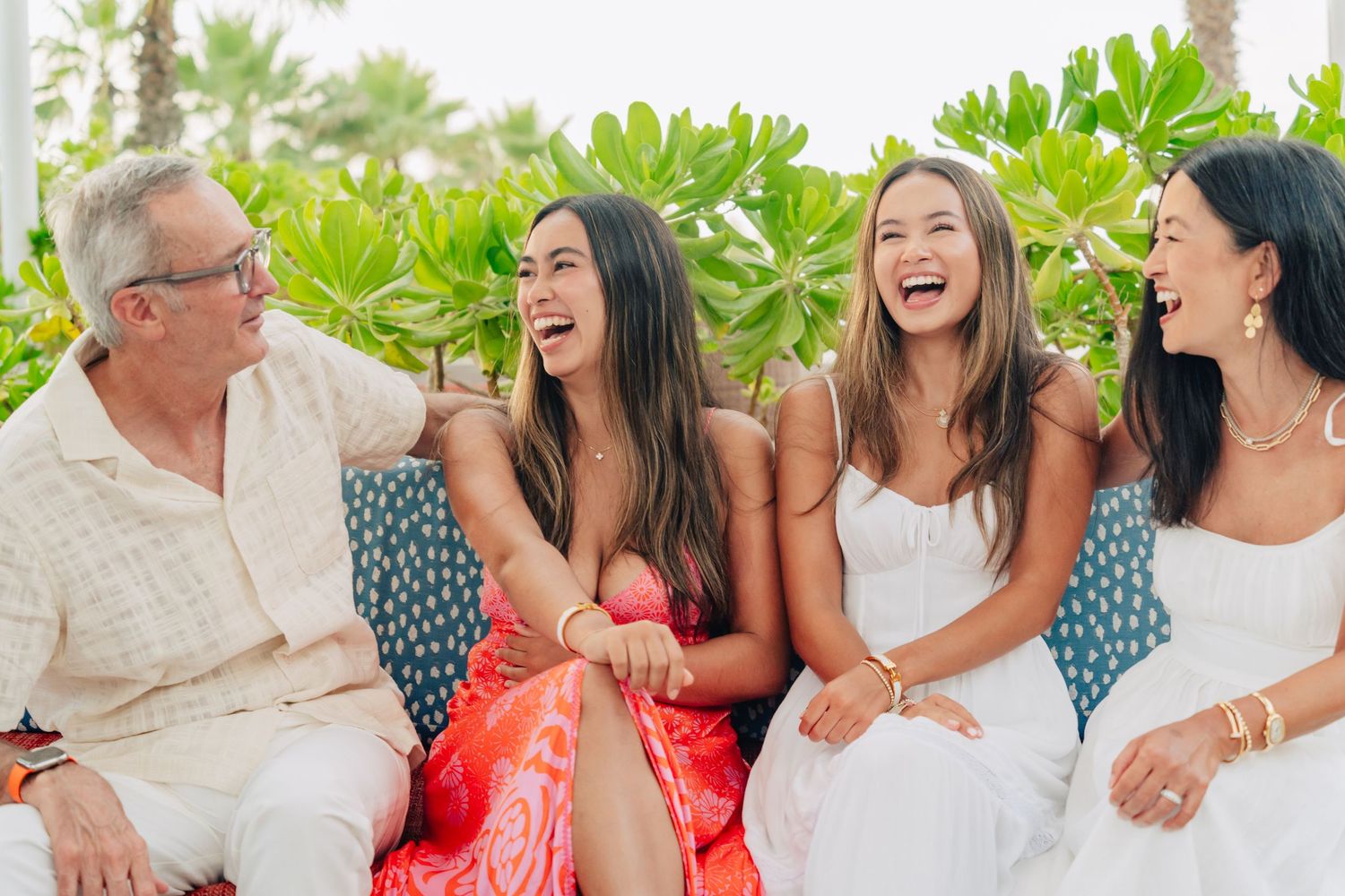 Joyful celebration outdoors with people in white and coral attire among tropical foliage.