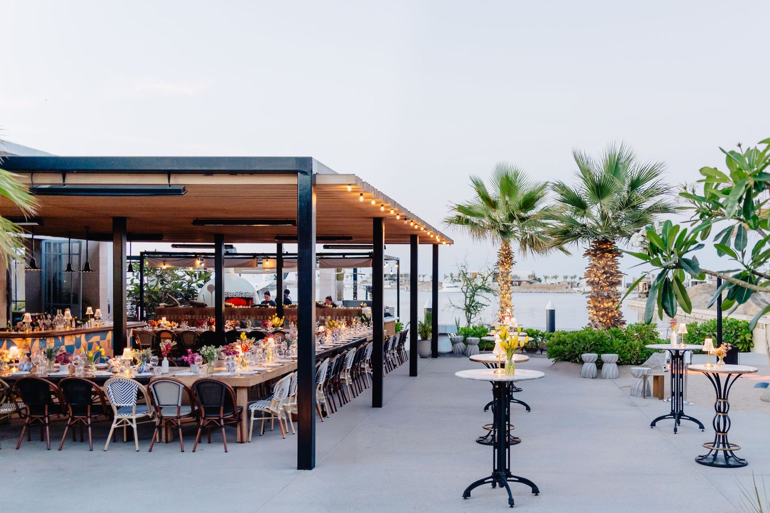 Modern outdoor restaurant terrace with palm trees and ocean view setting.