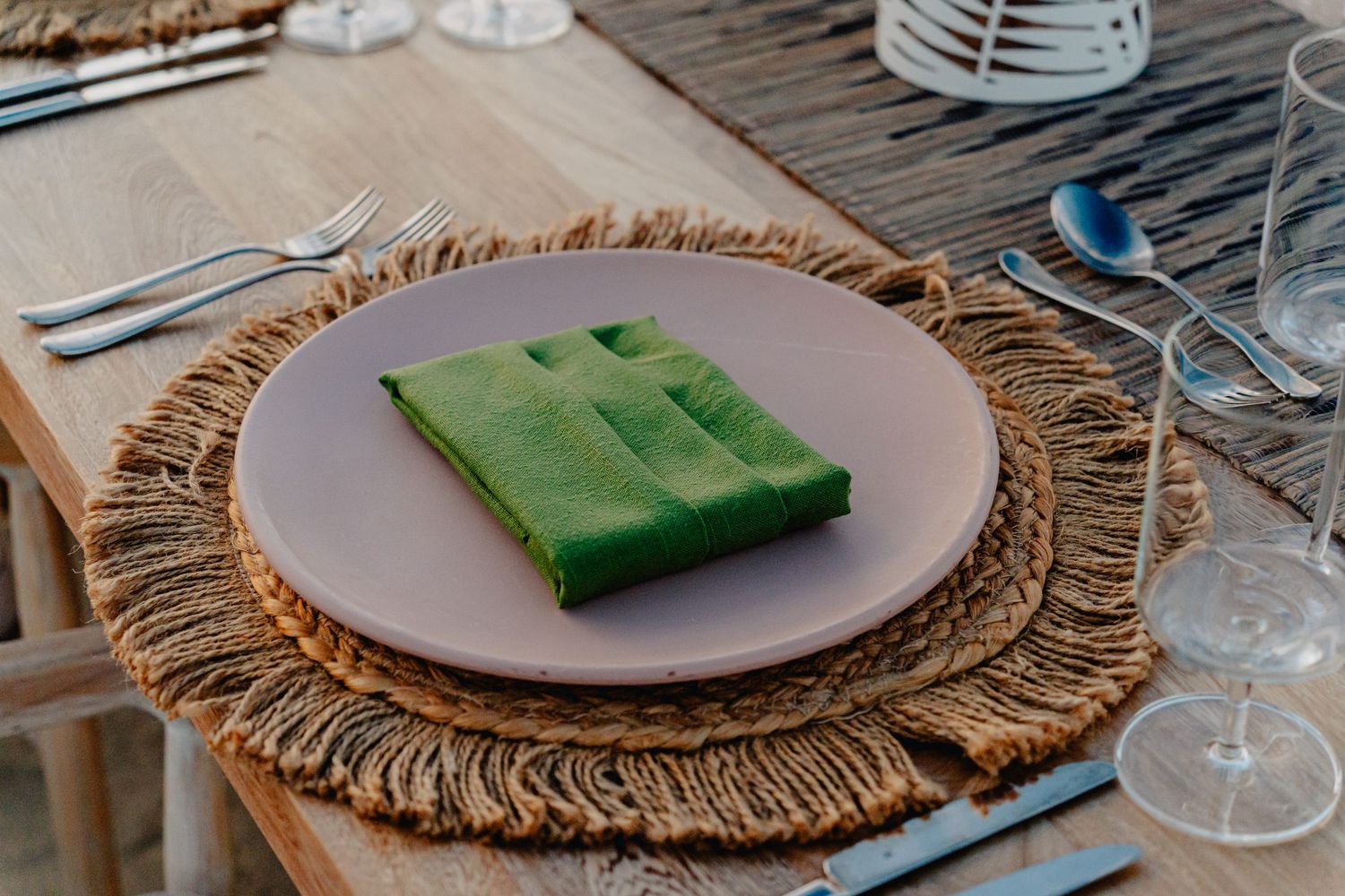 Elegant table setting with natural woven placemats and folded napkins on rustic wooden surface.