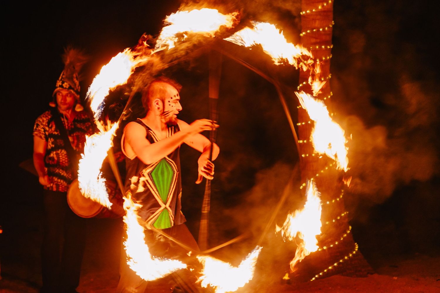 Fire performer spins flaming batons in a mesmerizing nighttime display creating circular patterns of light and flame.