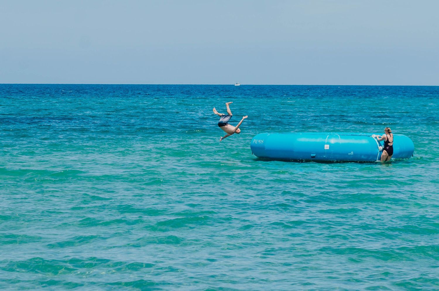 People jumping off an inflatable water trampoline in bright turquoise ocean waters.