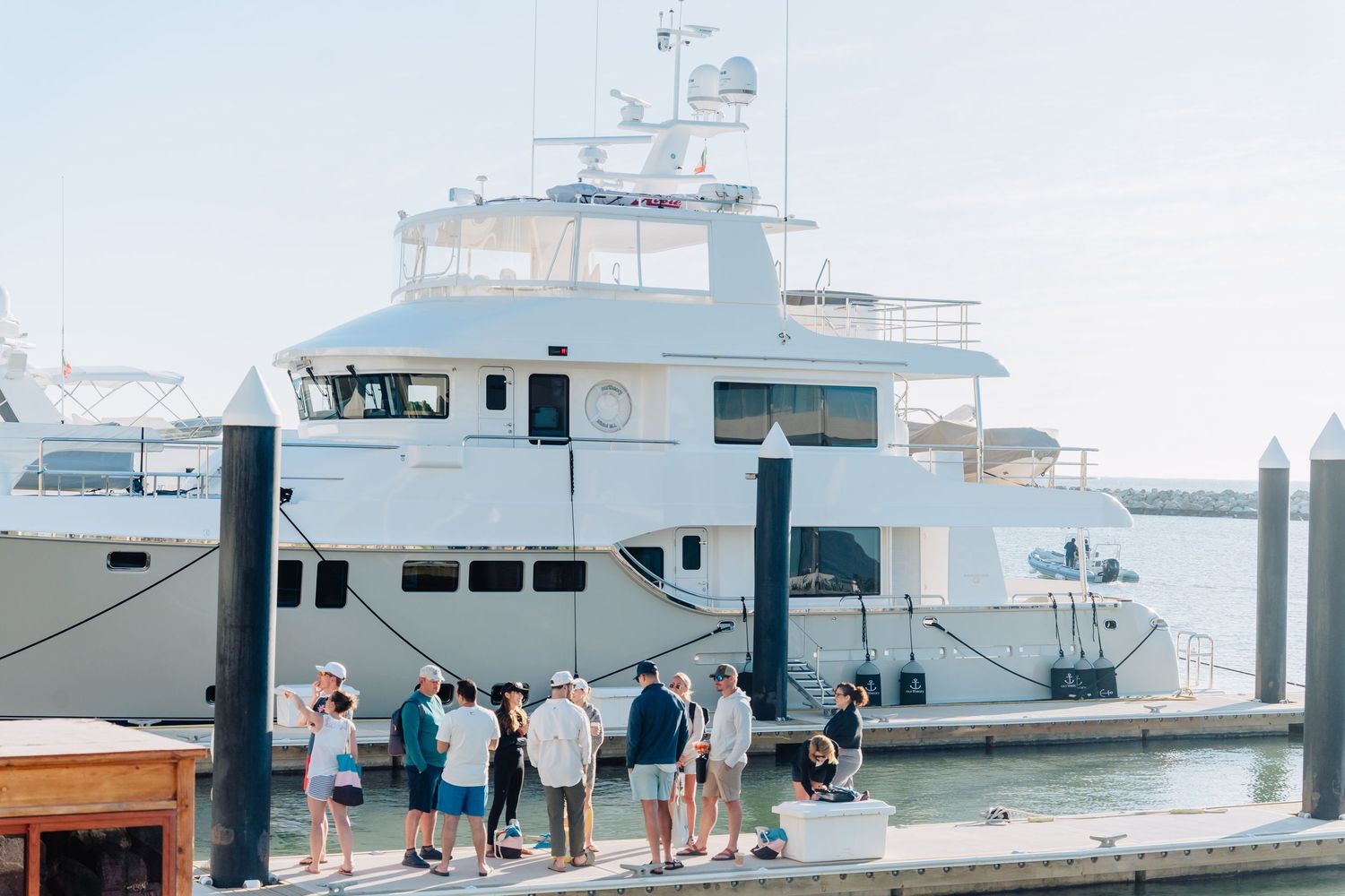 Large luxury yacht docked at marina with group of visitors on the dock.