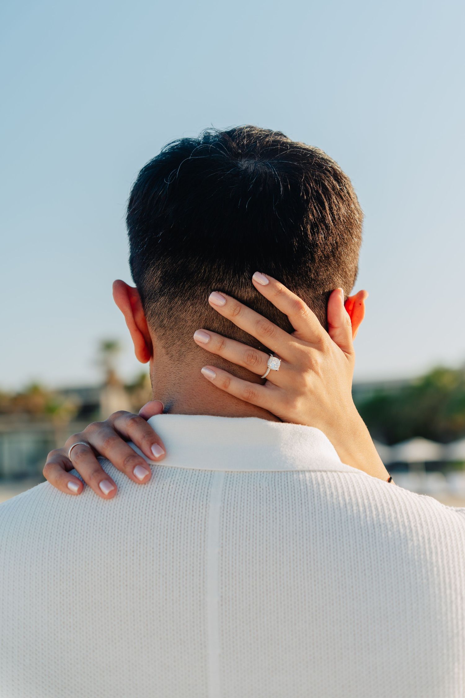 A close-up view of someone's head from behind with a hand wearing a ring resting on their neck.
