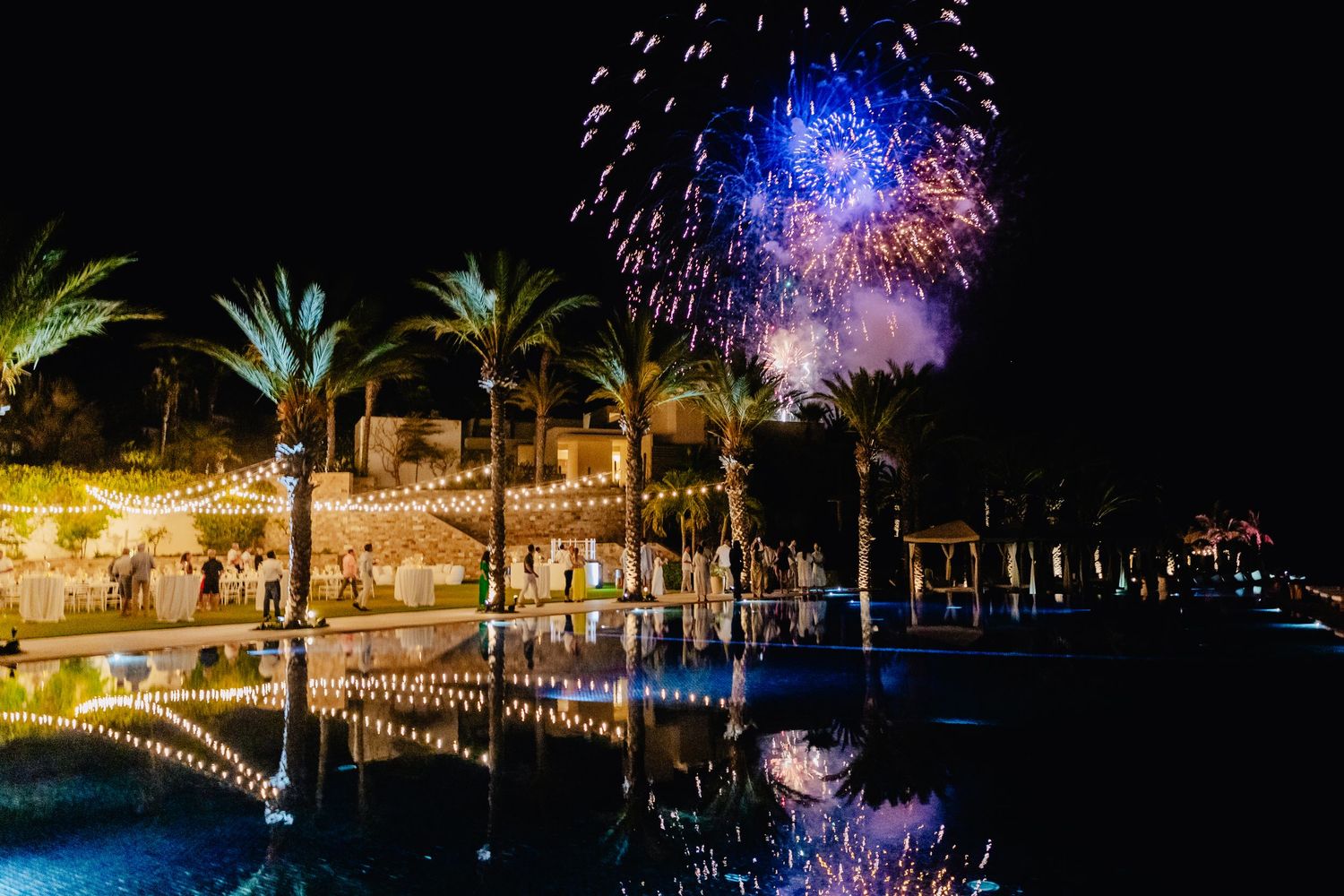 Nighttime celebration with fireworks illuminating palm trees and a pool area at a luxurious tropical resort.