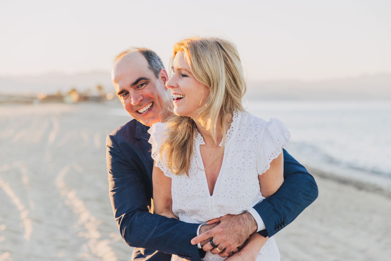 Couple shares tender moment together on sandy beach at sunset with soft lighting and ocean backdrop.
