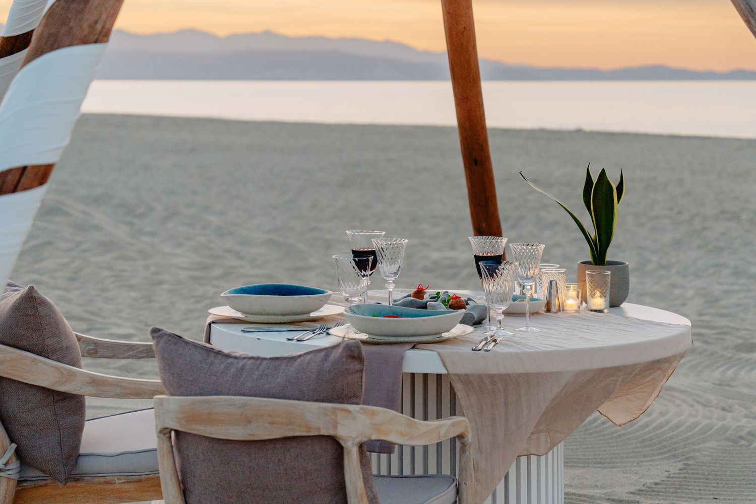Coastal dining setup with white tablecloth, wicker chairs, and ocean view on a sunny day.