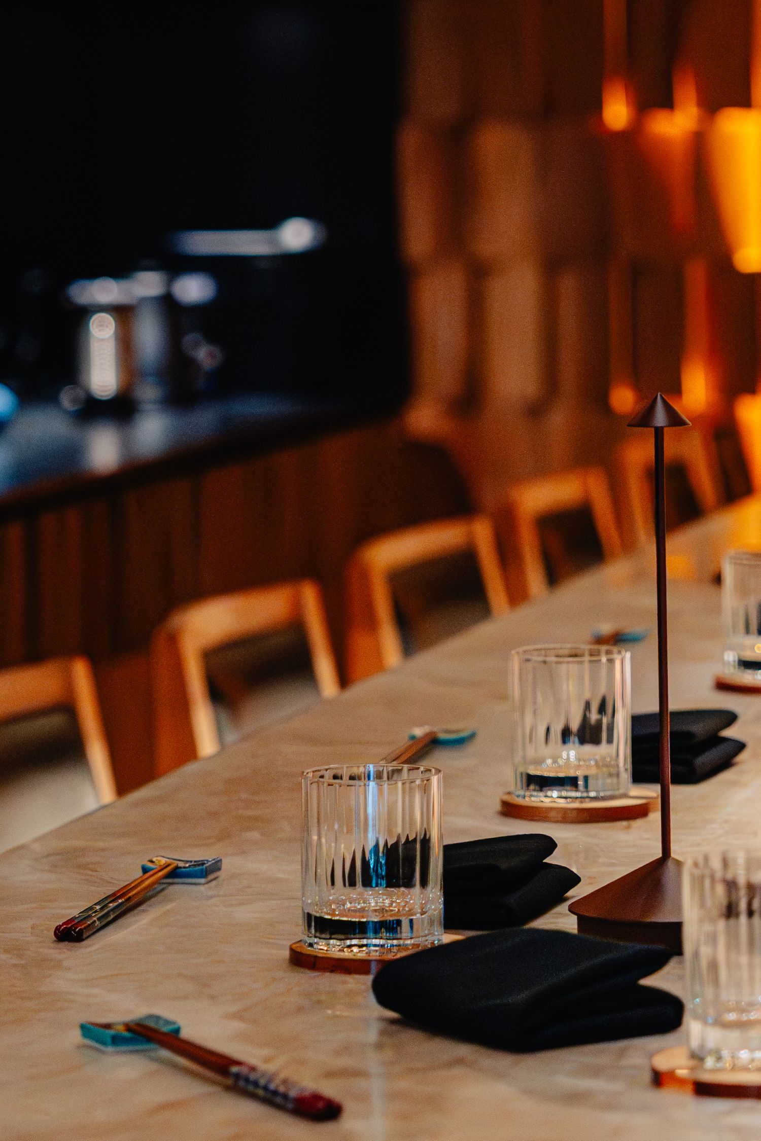 Restaurant table setting with glasses, black napkins and cutlery arranged in dim lighting with warm ambiance.