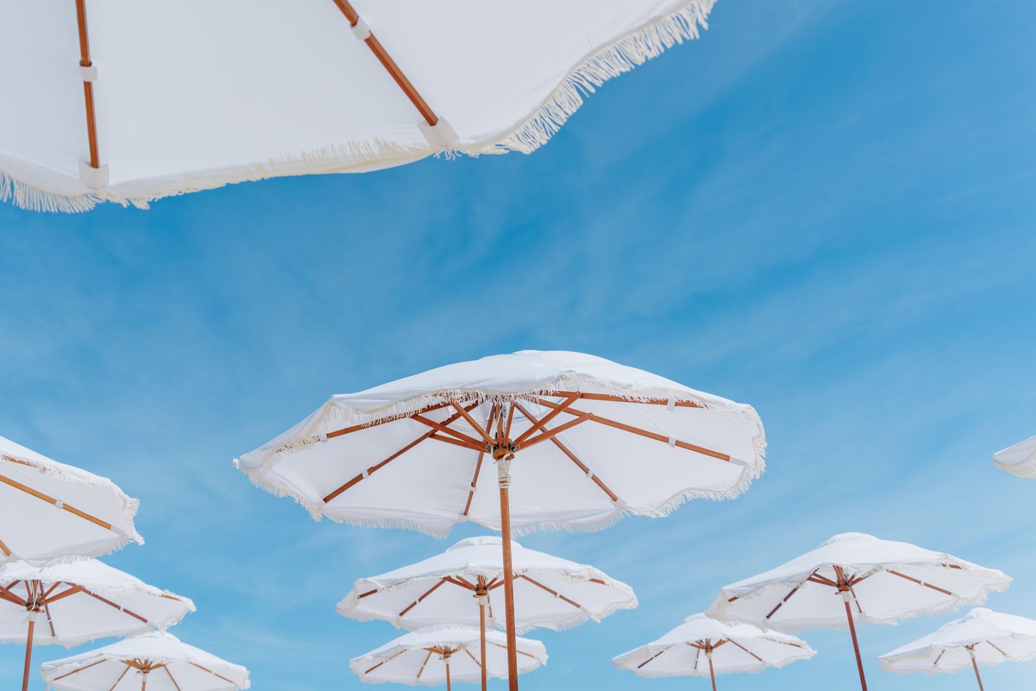 White beach umbrellas against bright blue sky create a summer resort atmosphere.