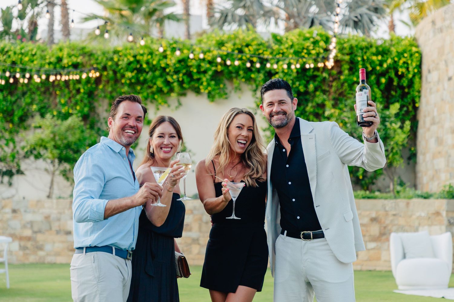 Party guests enjoying drinks and conversation during a sunset outdoor celebration.