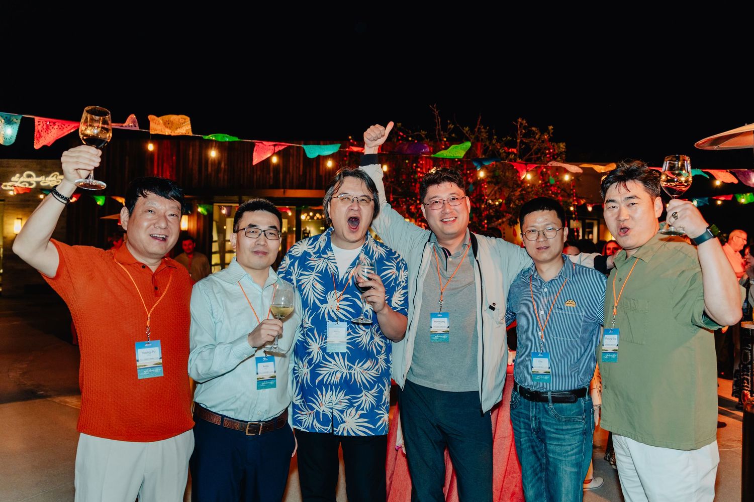 A group of people gathered at a nighttime event with colorful banners and lighting in the background.
