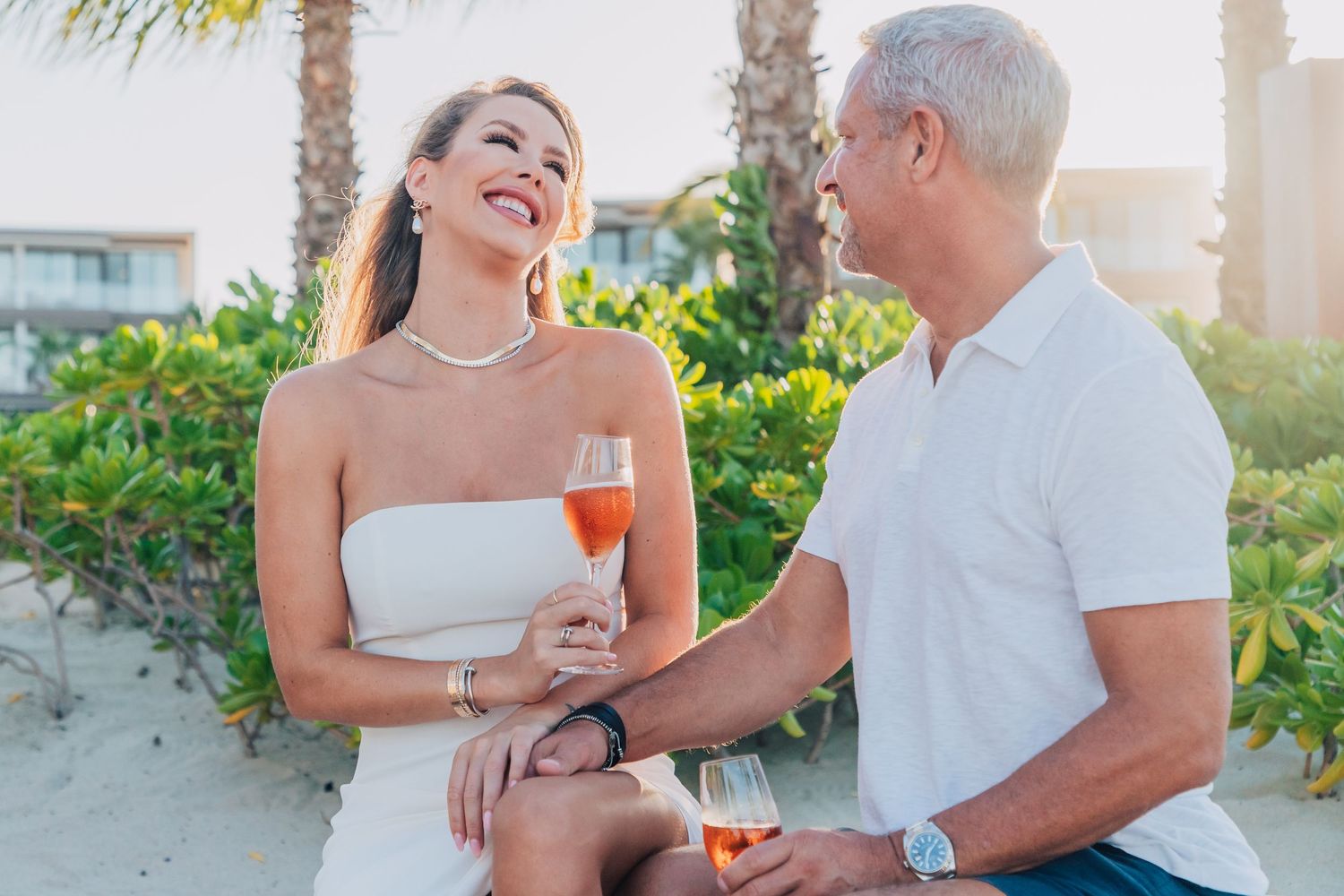 Couple celebrating with champagne on a palm-lined beach at sunset.