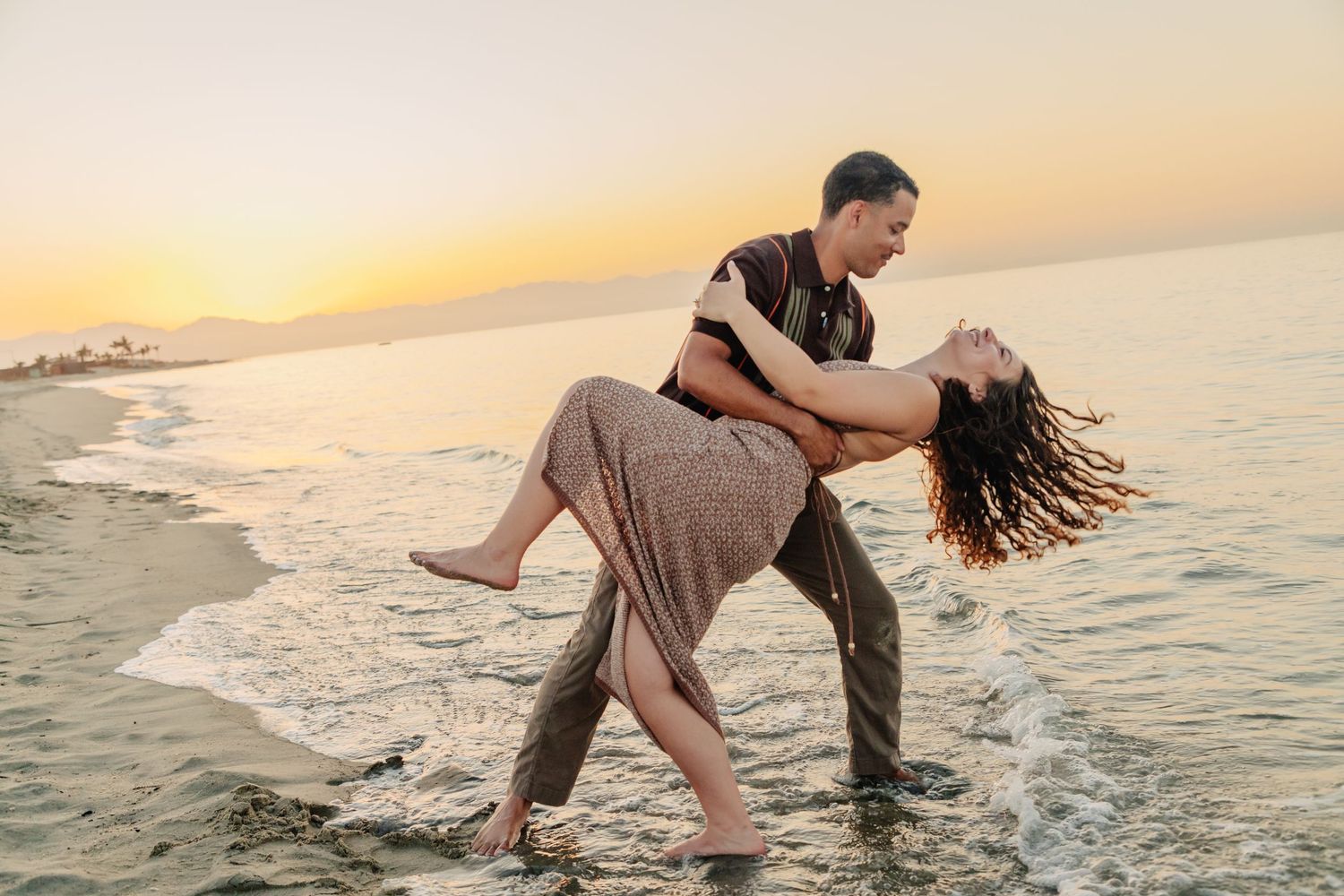 A couple dances together in the ocean waves during a romantic sunset photoshoot at the beach.