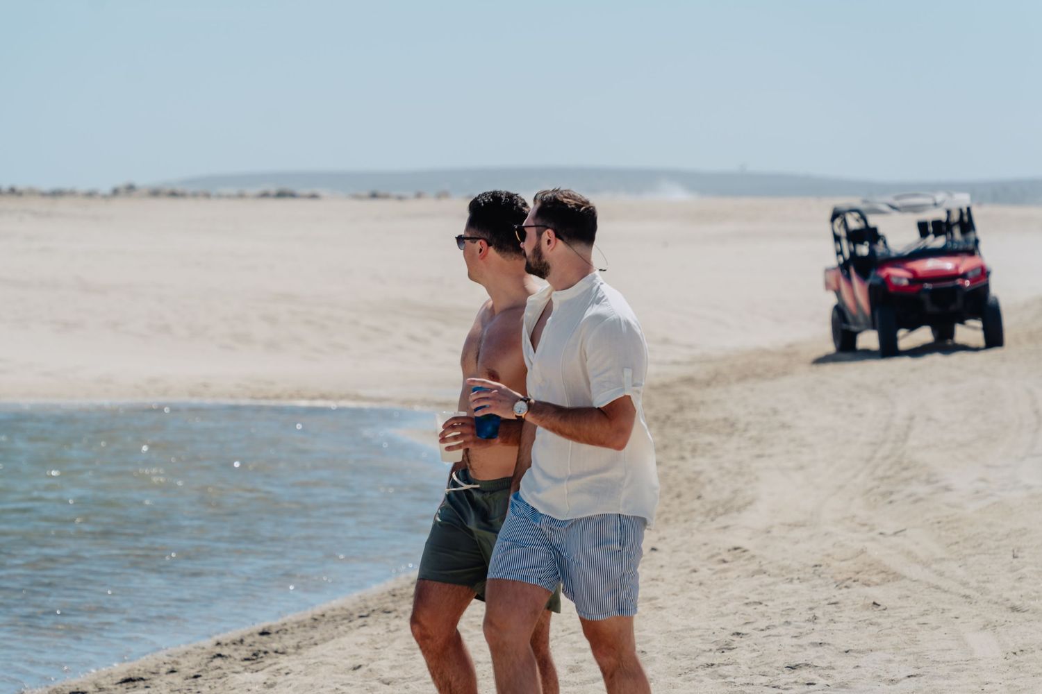 A couple shares an intimate moment on a beach with an off-road vehicle visible in the background.
