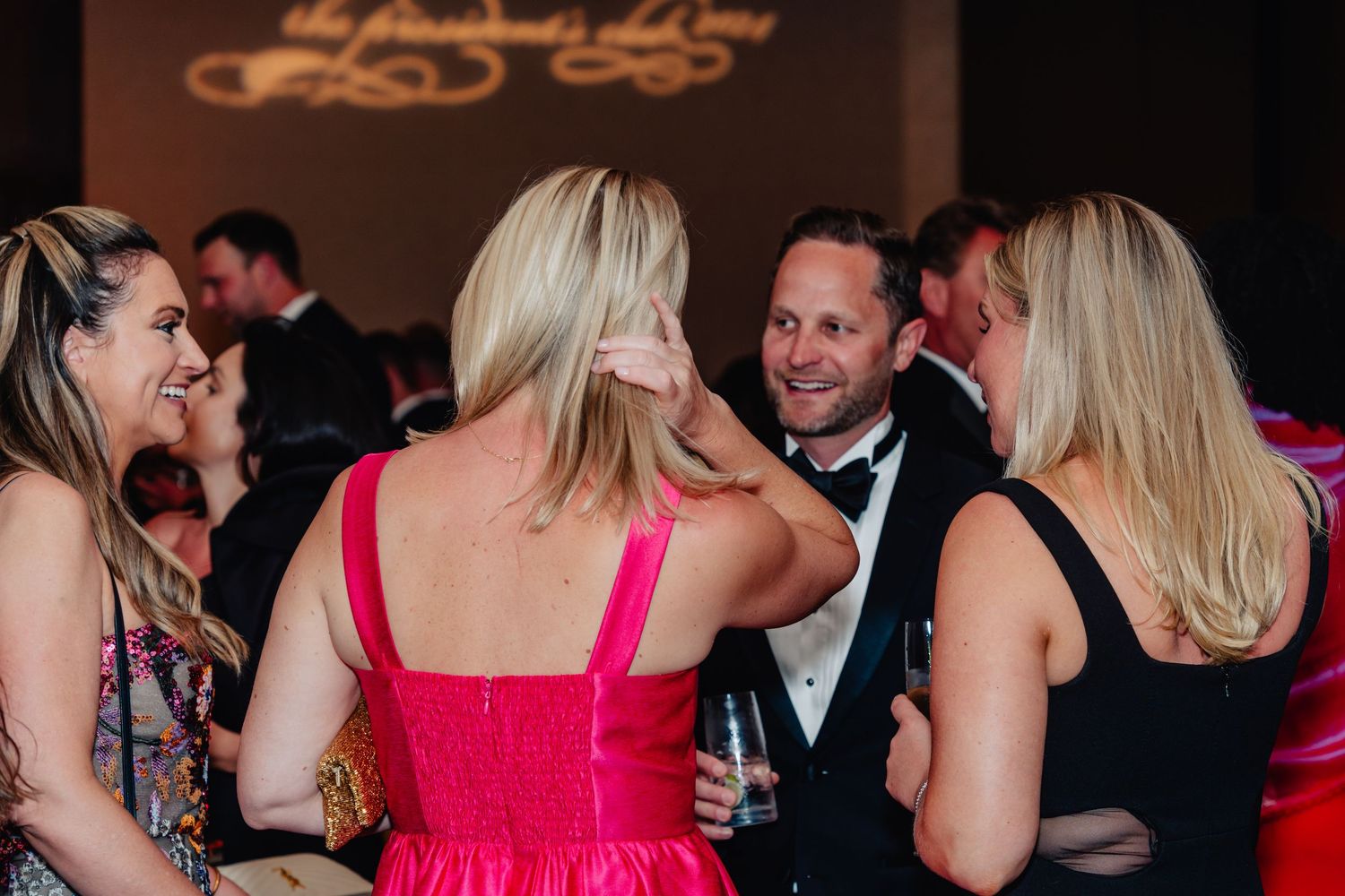 Guests in formal attire dancing and socializing at an elegant evening reception with pink and red accents.
