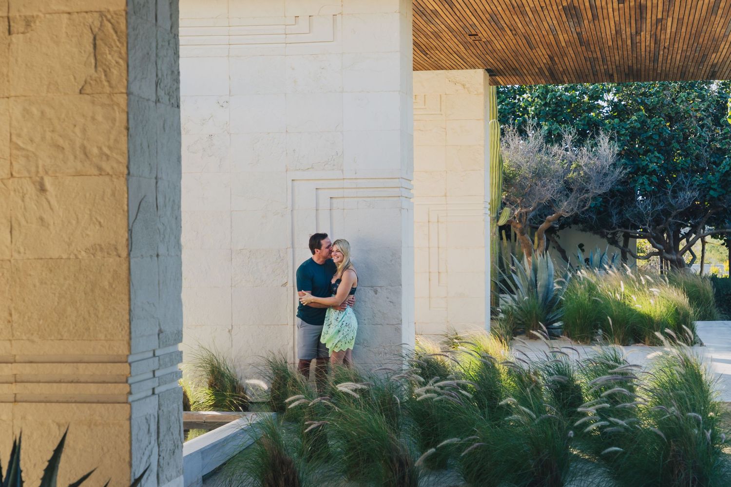 A series of outdoor engagement photos taken under a covered walkway with stone columns and lush greenery.