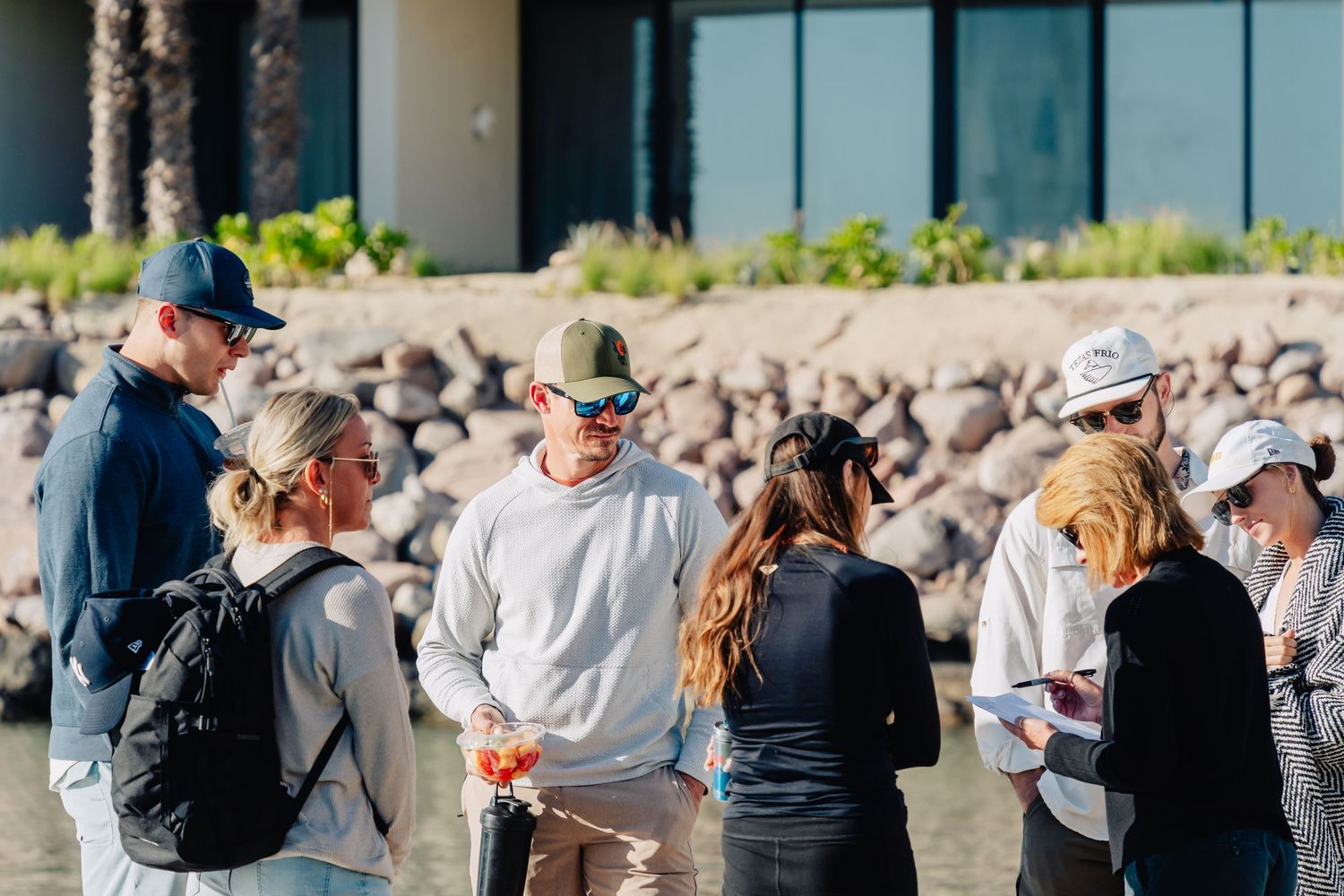 A crowd of people waiting in line outside a glass building on a sunny day.