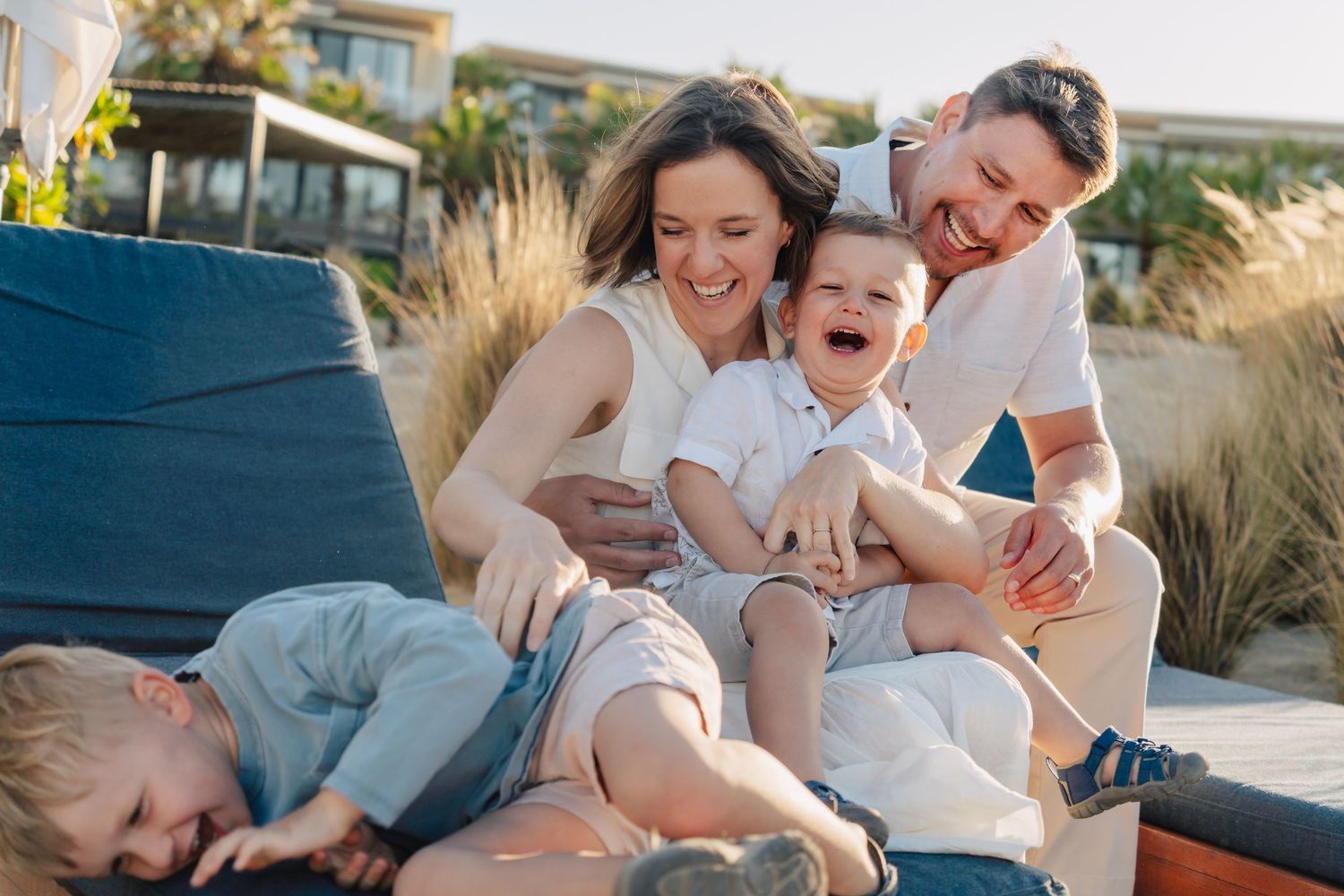 A relaxed family moment on an outdoor lounge chair surrounded by coastal vegetation.