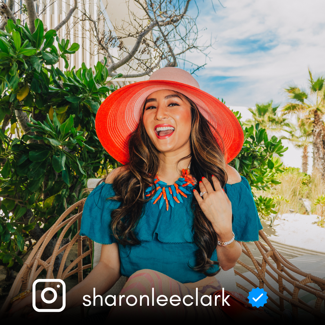 Person wearing a bright red sunhat enjoying a sunny day among tropical foliage.
