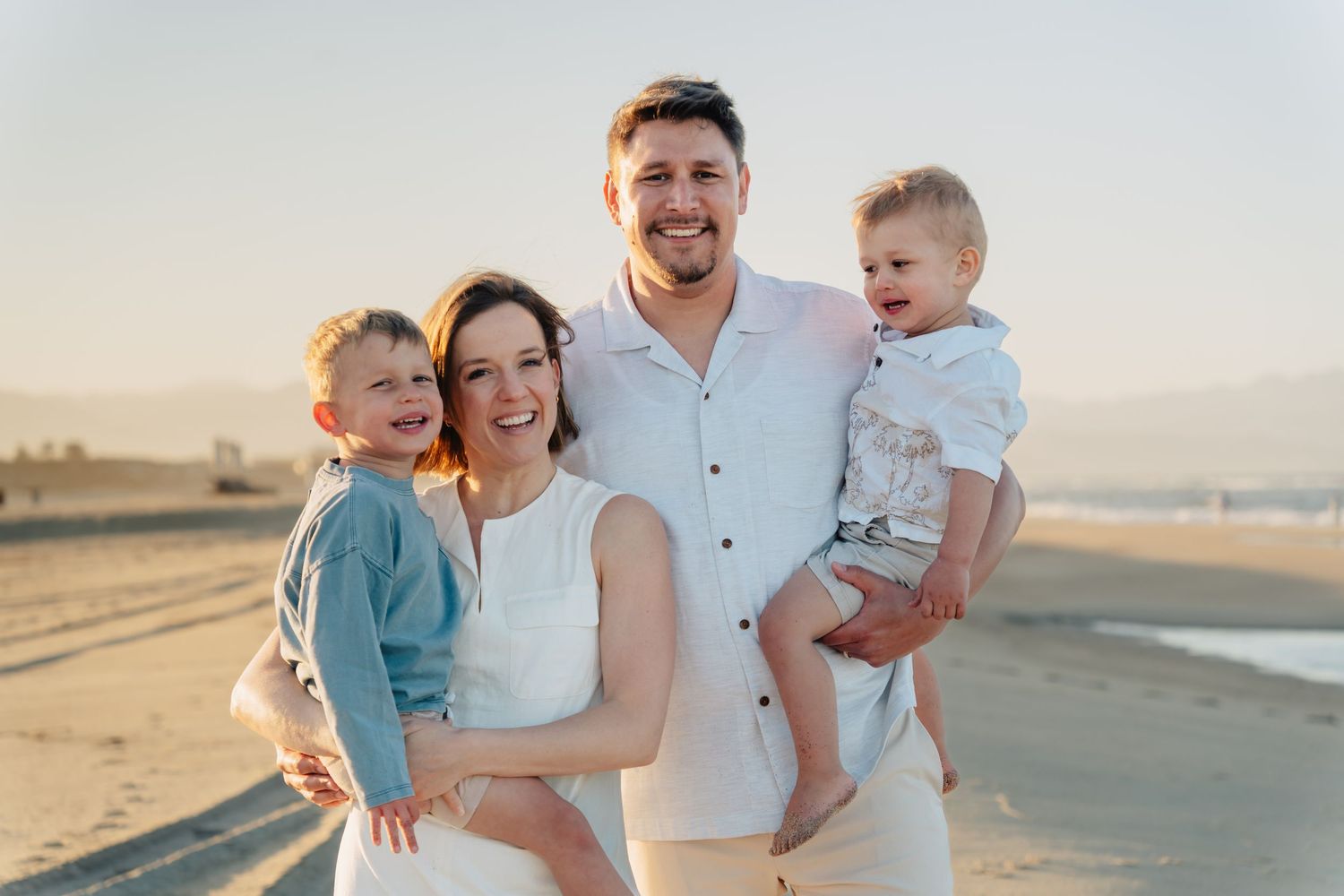 A family poses together on a sandy beach during golden hour.