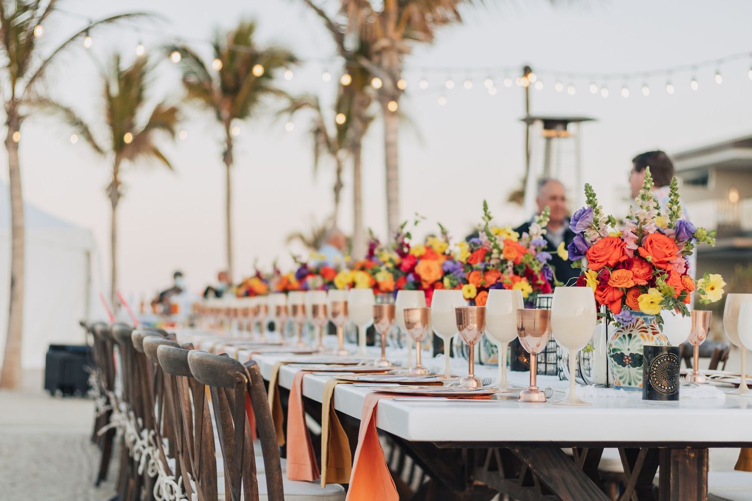 Elegant outdoor wedding reception table with tropical floral centerpieces and palm trees.