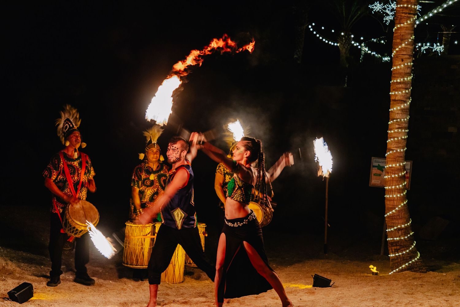 Fire performers entertain guests with flaming torches against the night sky.