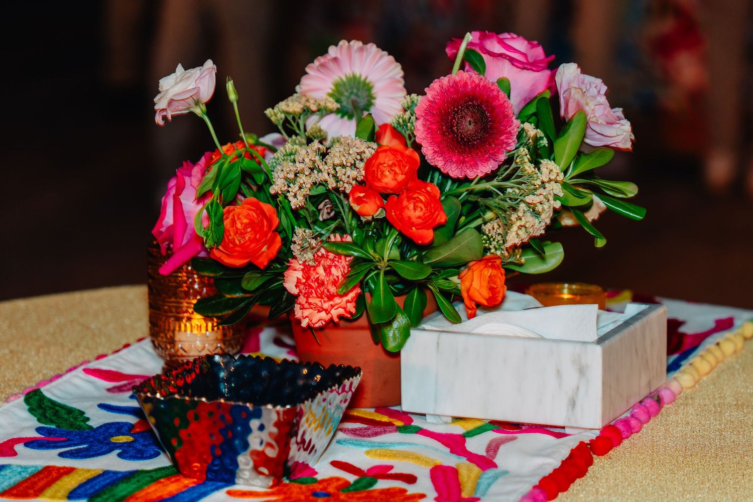 Vibrant pink and orange floral centerpieces with roses decorate a rustic wooden table at an event.