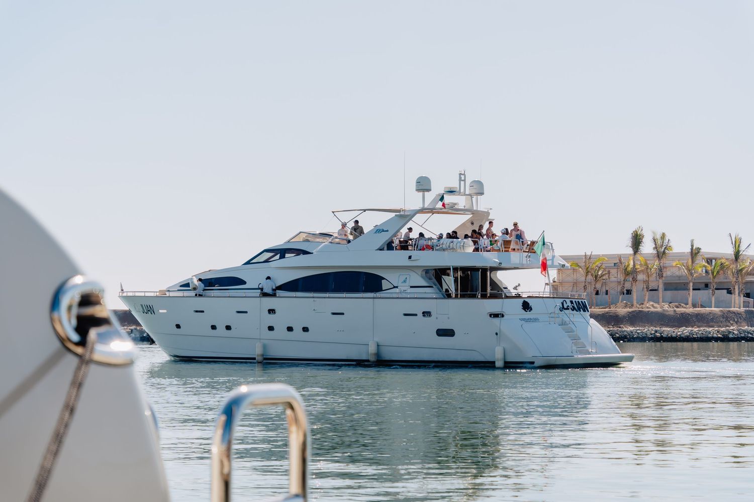 Luxury yacht cruising along a Mediterranean coastline with passengers enjoying the sunny day at sea.