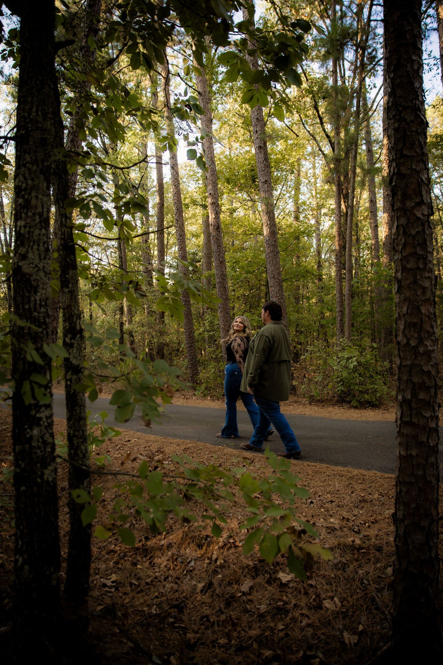 Couple walking down road amongst forrest scenery smiling at eachother