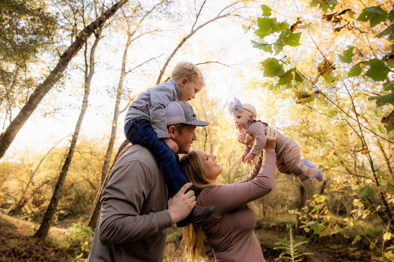 Family with boy on Dad's shoulder and mom holding baby in air