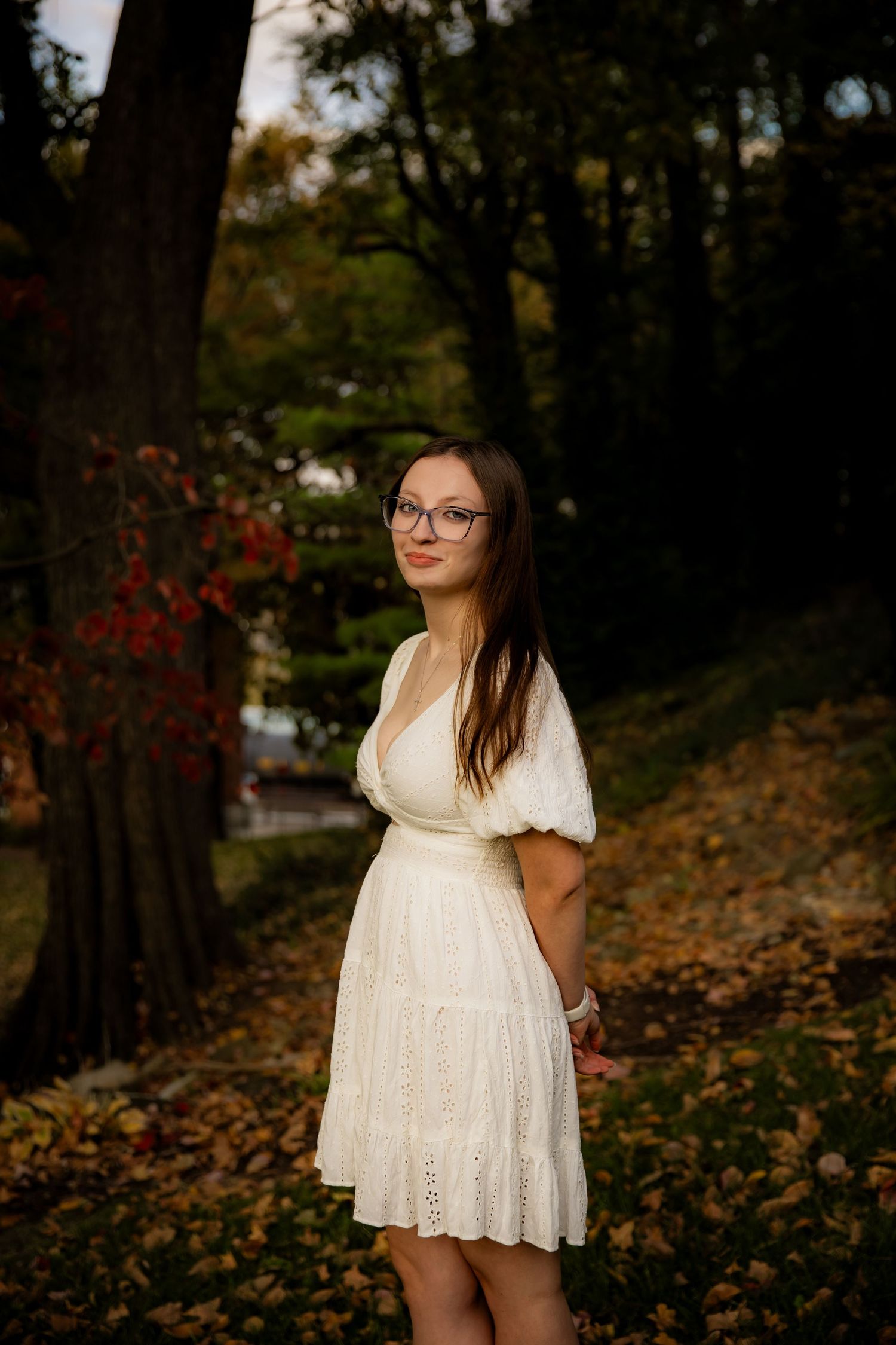 Girl standing in fall leaves and smiling at camera in white dress