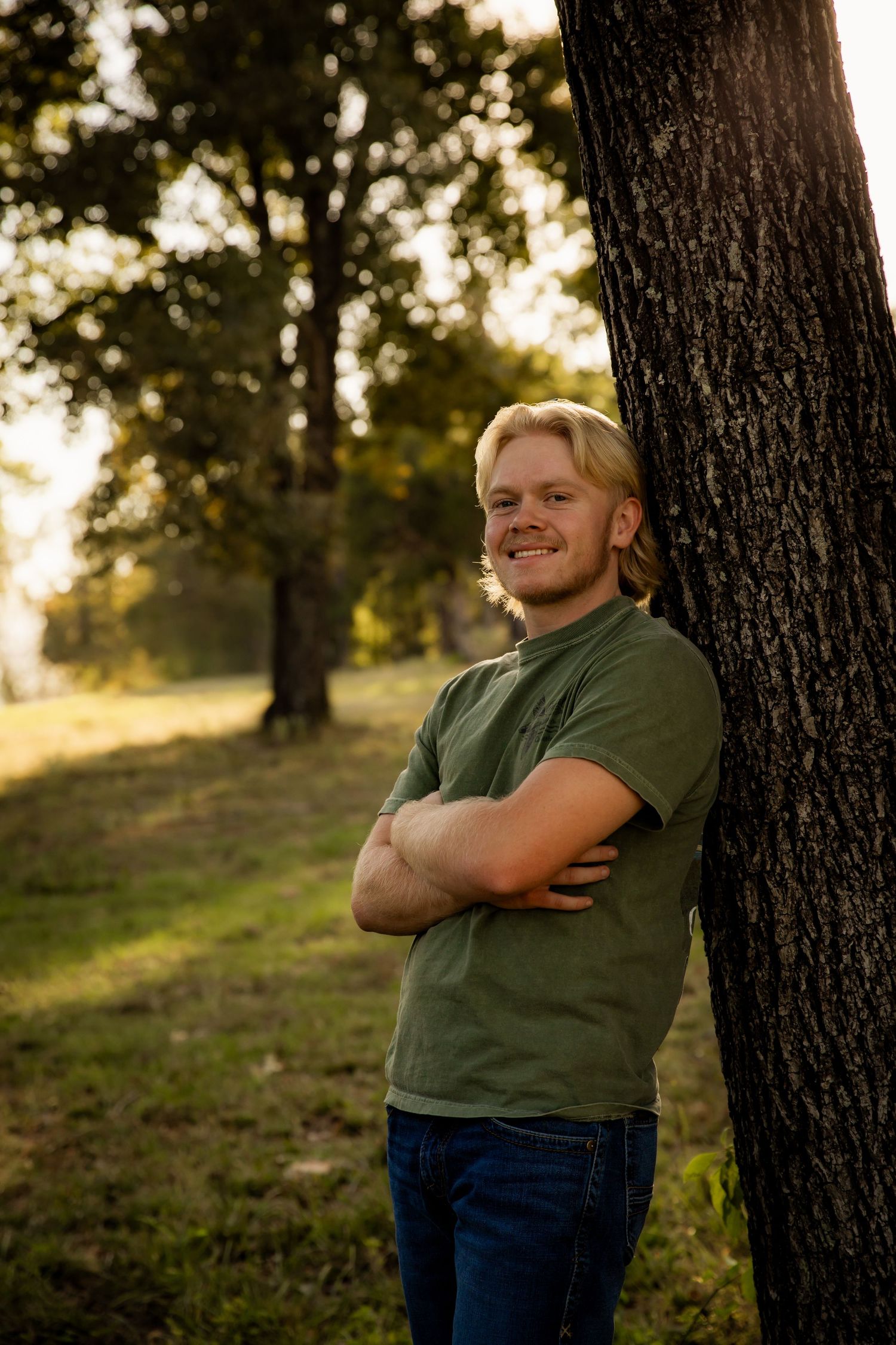 Boy leaning against tree smiling with arms crossed