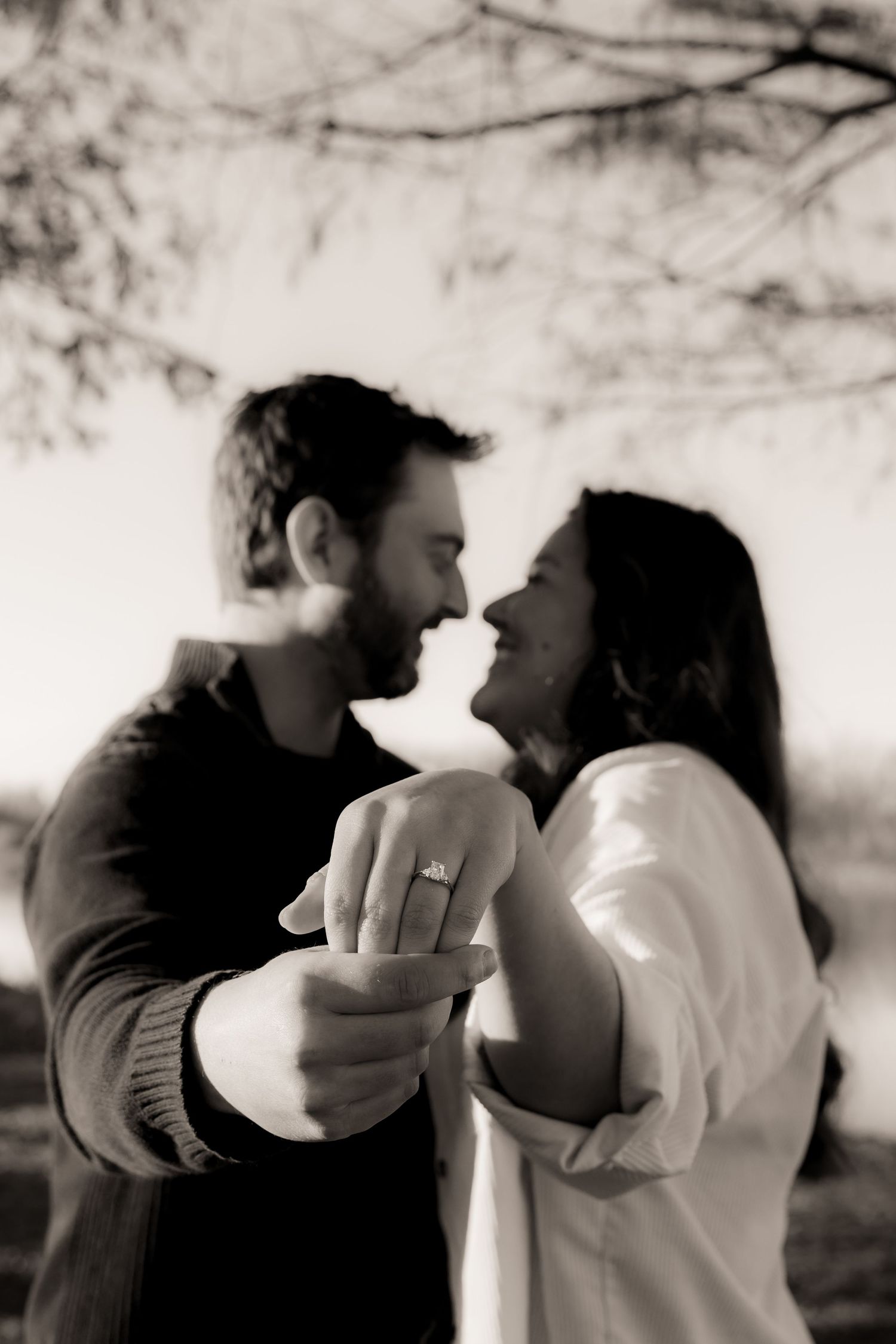 Holding hand out towards camera to show off engagement ring and smiling at each other