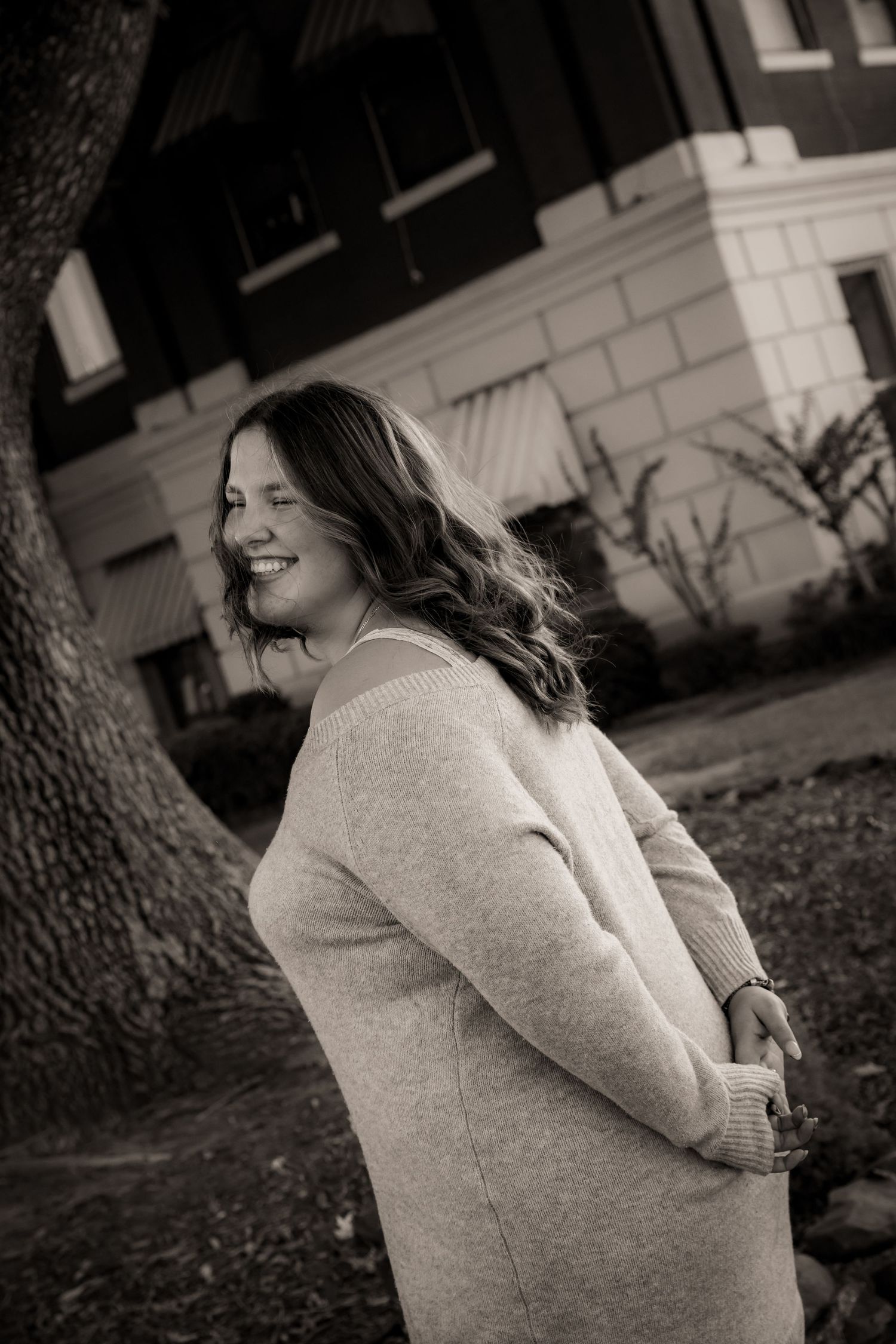 Girl holding hands behind back and laughing black and white