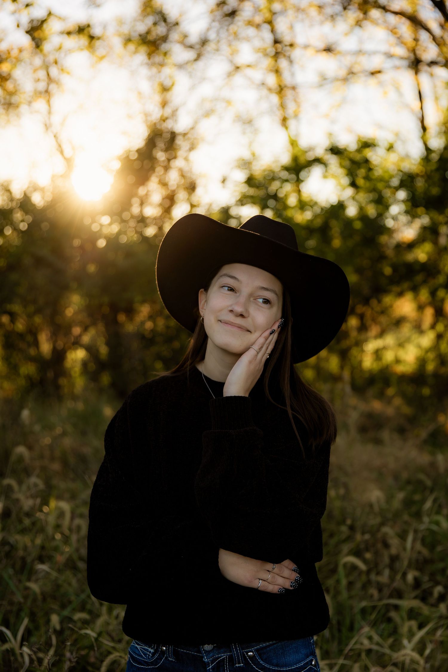 Girl with cowboy had with hand on cheek looking off and smiling