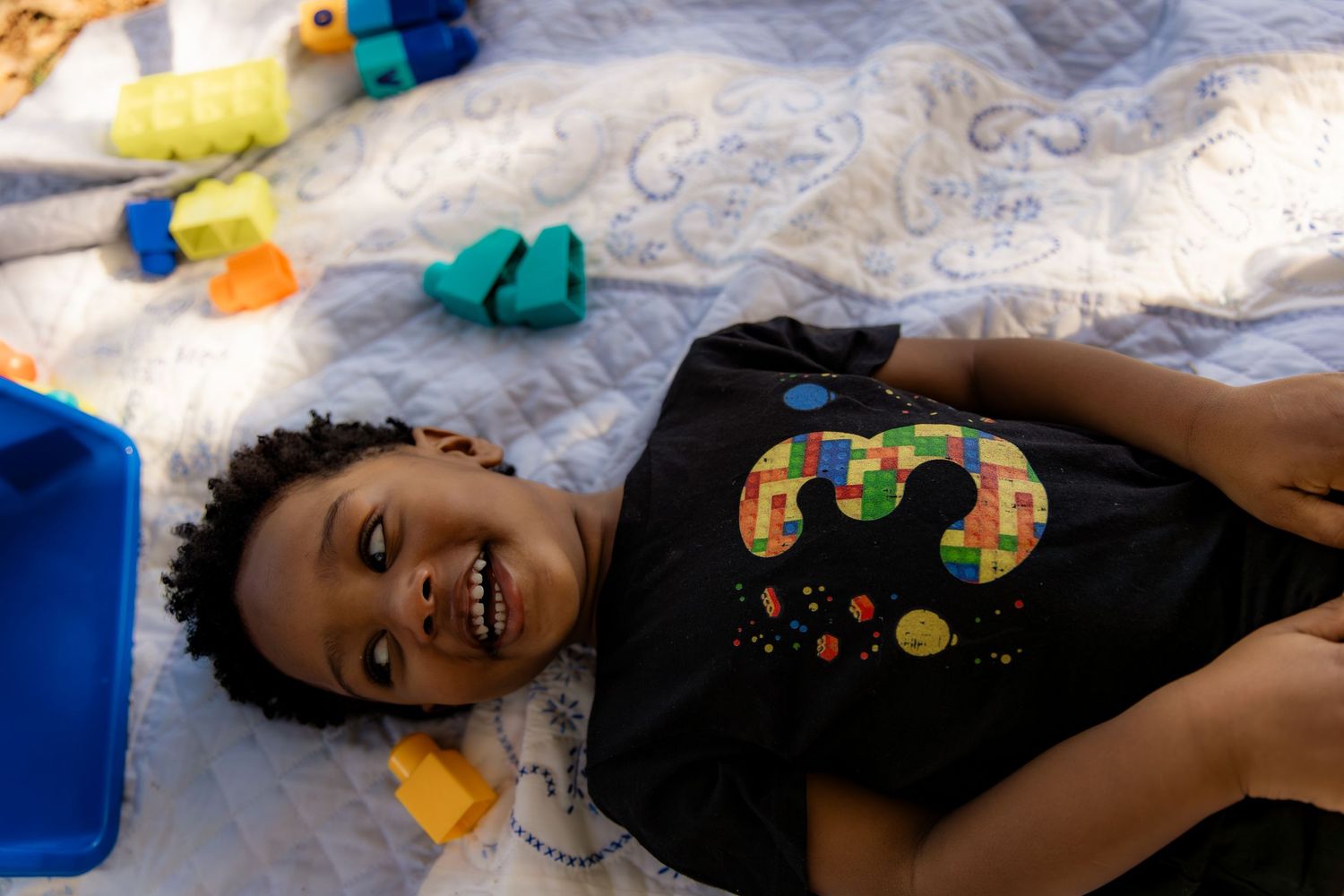 Boy laying on quilt surrounding by blocks and smiling