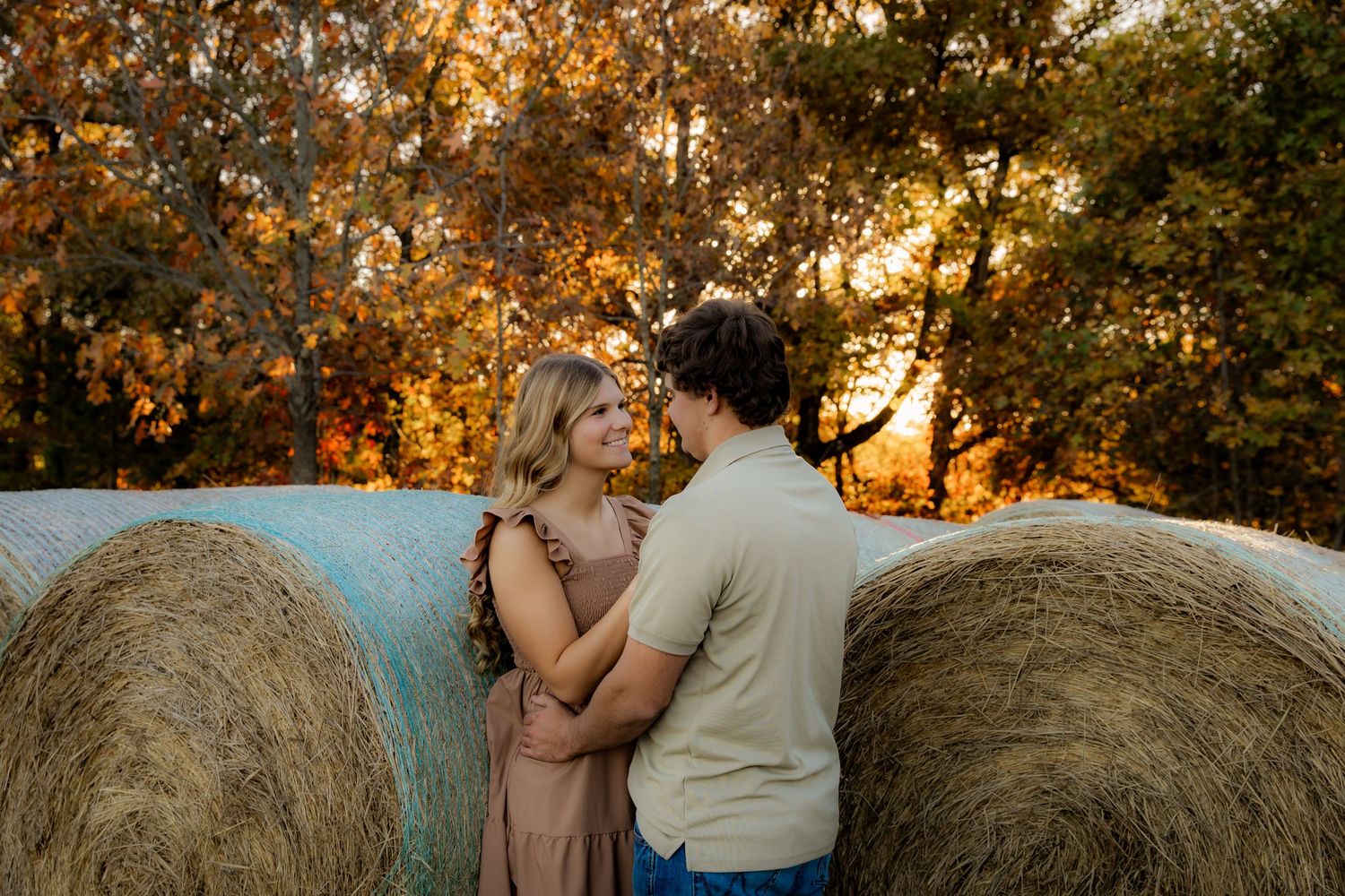 Boy and girl in front of haybales with fall leaves smiling at eachother