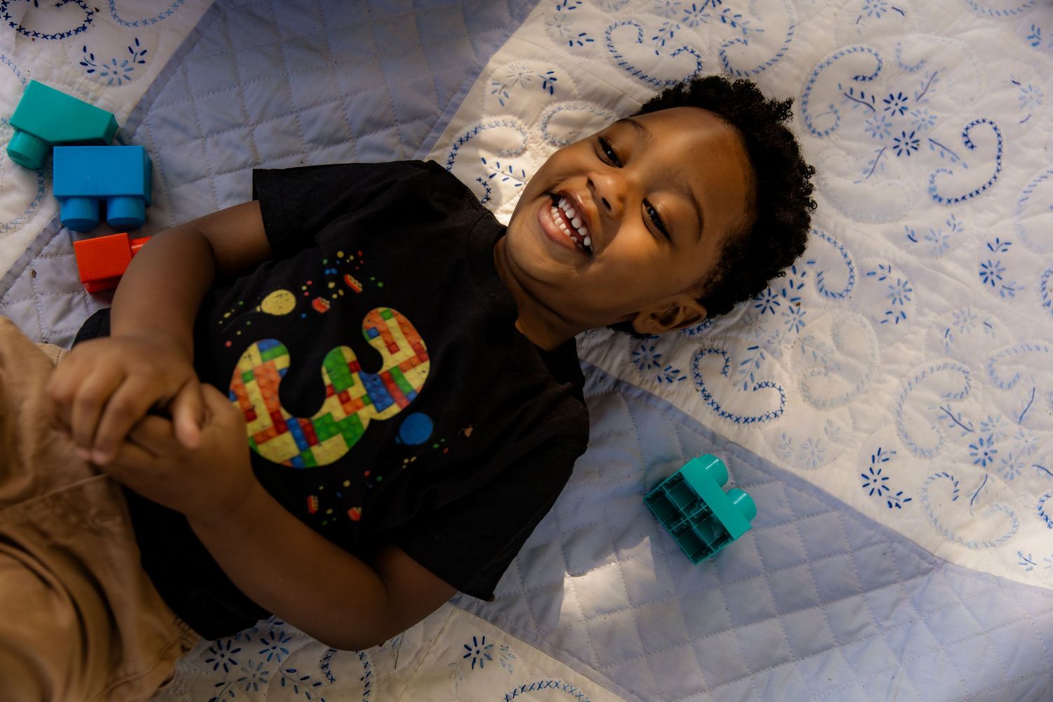 Boy laying on quilt with blocks around him laughing