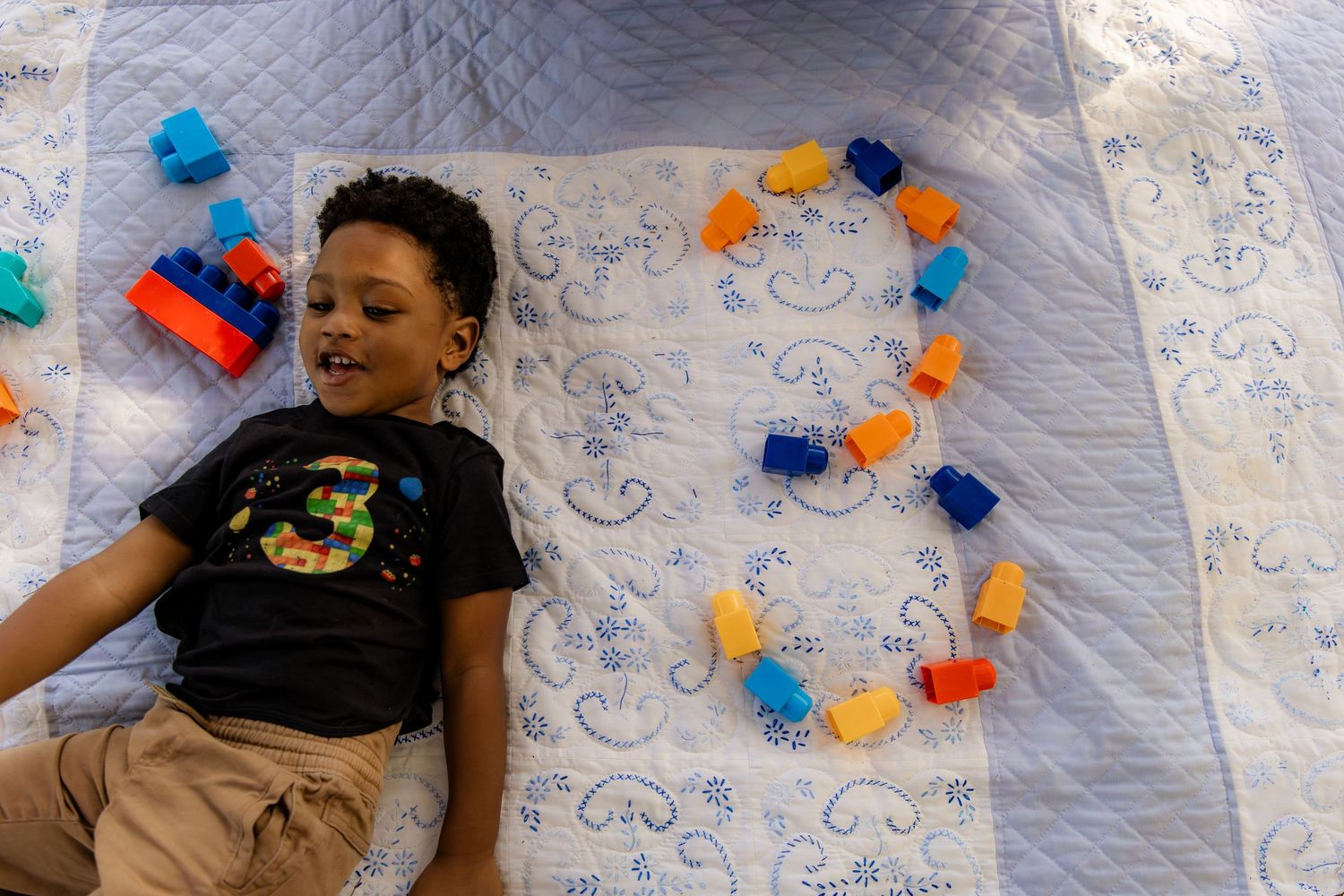 Boy laying next to number three made with blocks on quilt