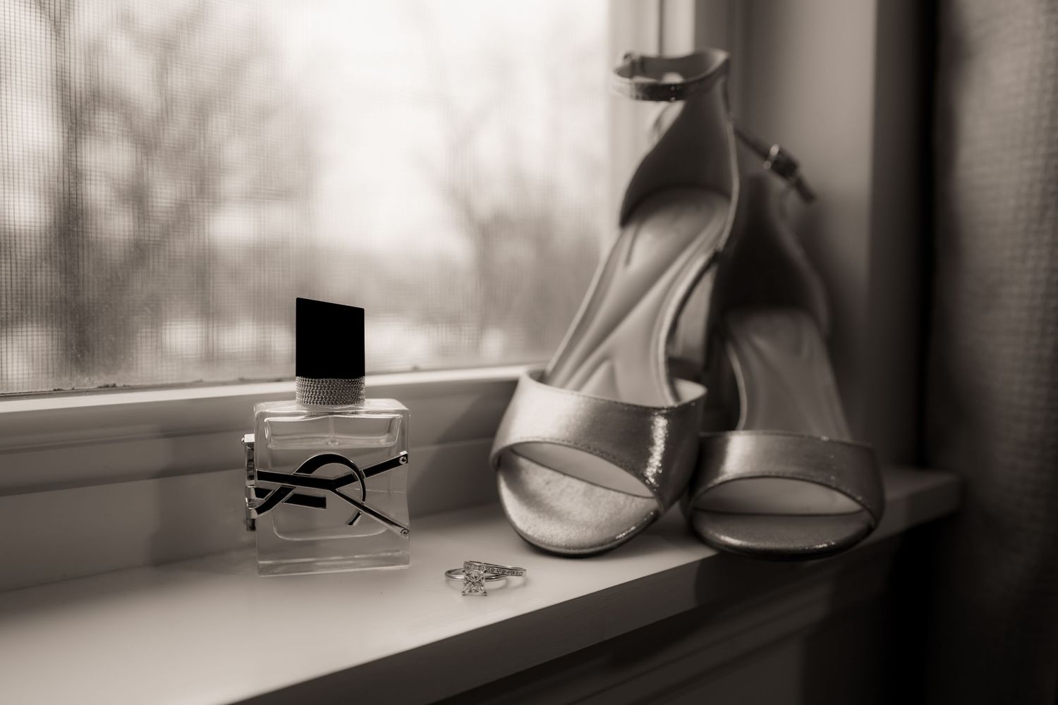 Shoes in window with perfume and engagement ring black and white