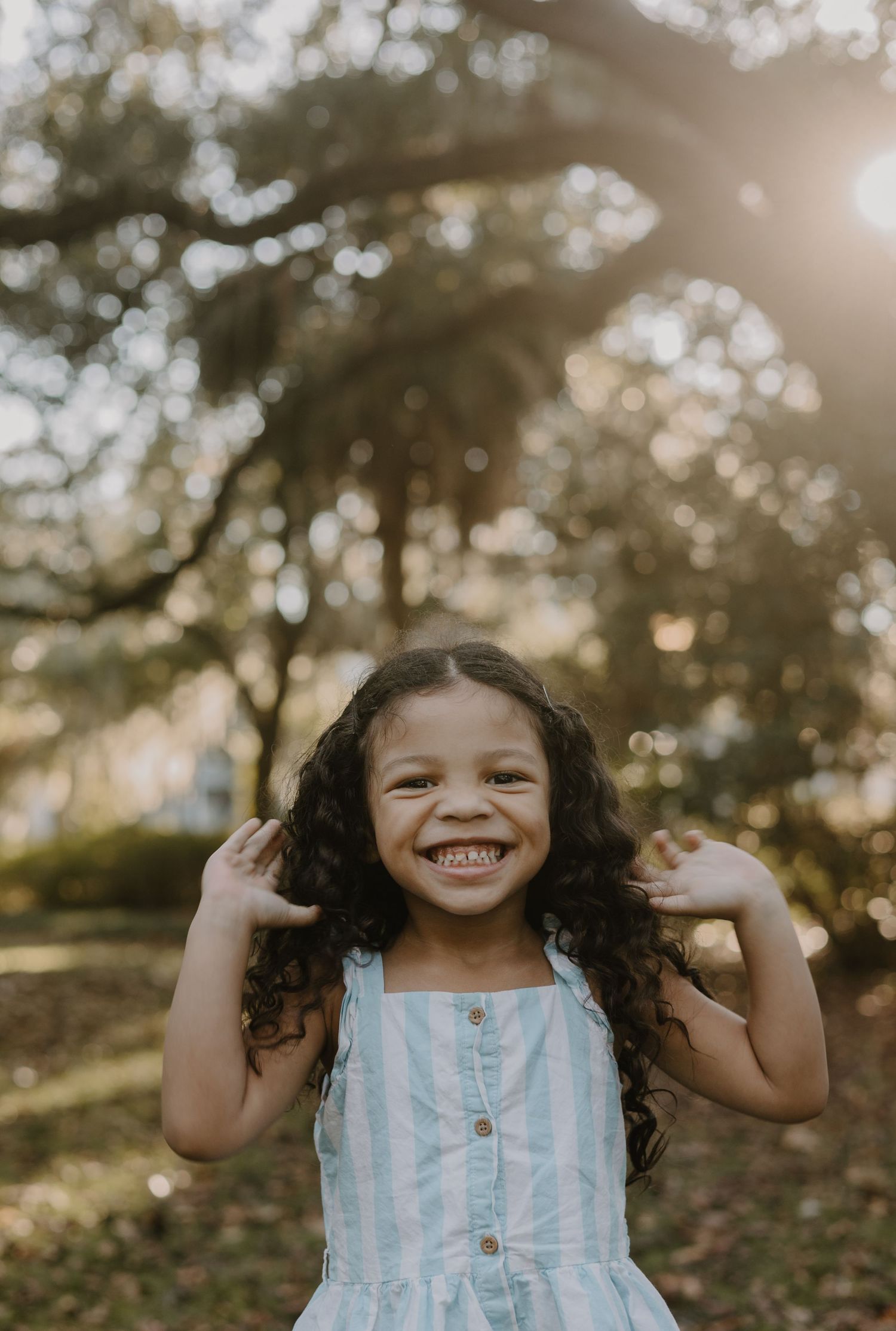 Child in a blue and white striped dress plays joyfully outdoors during golden hour.