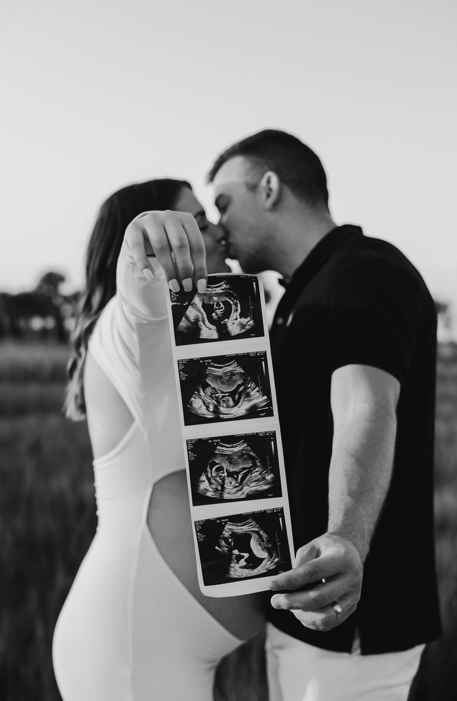 Black and white photo of a couple sharing ultrasound photos during a pregnancy announcement.