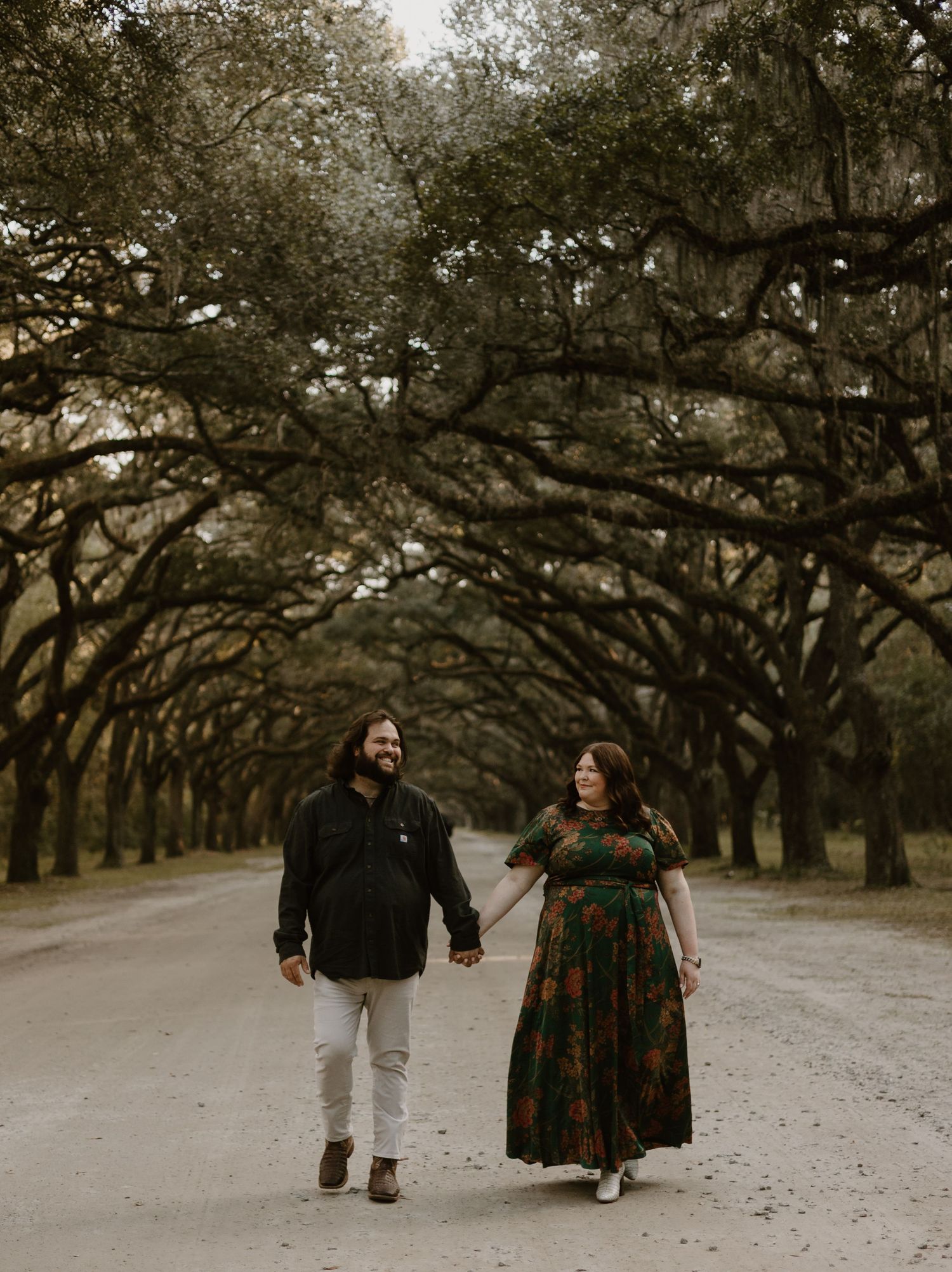 A couple walks hand in hand down a tree-lined path in winter.