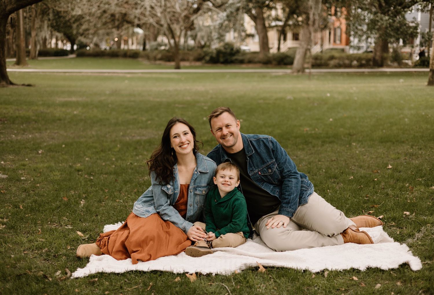Family lying on white blanket outdoors during autumn photo session in park.