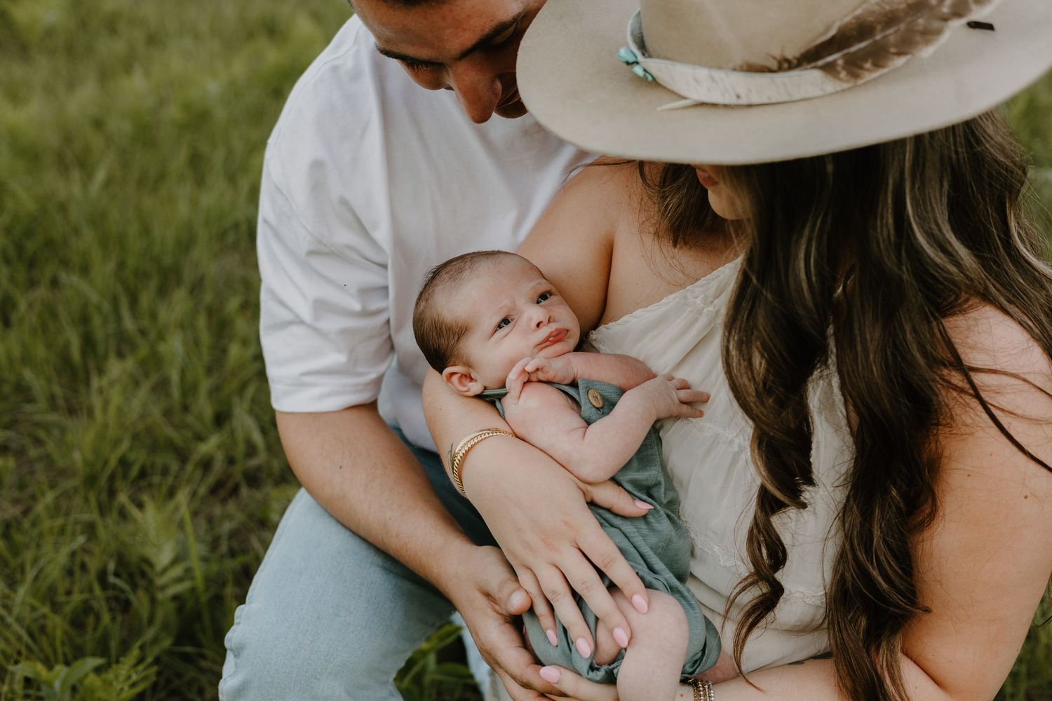 A family shares tender moments together while sitting in green grass during an outdoor photoshoot.