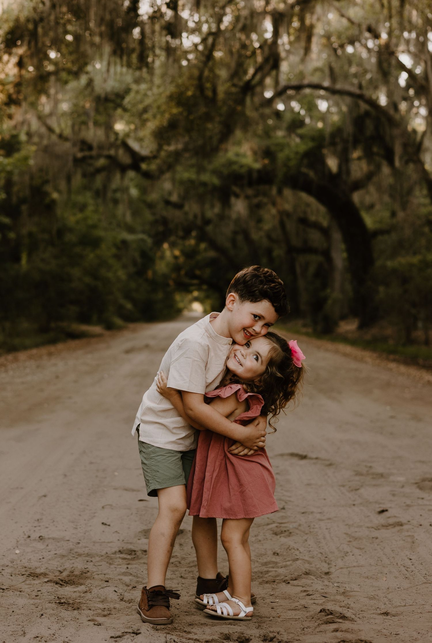 Two children sharing a sweet moment on a dirt path in natural lighting.