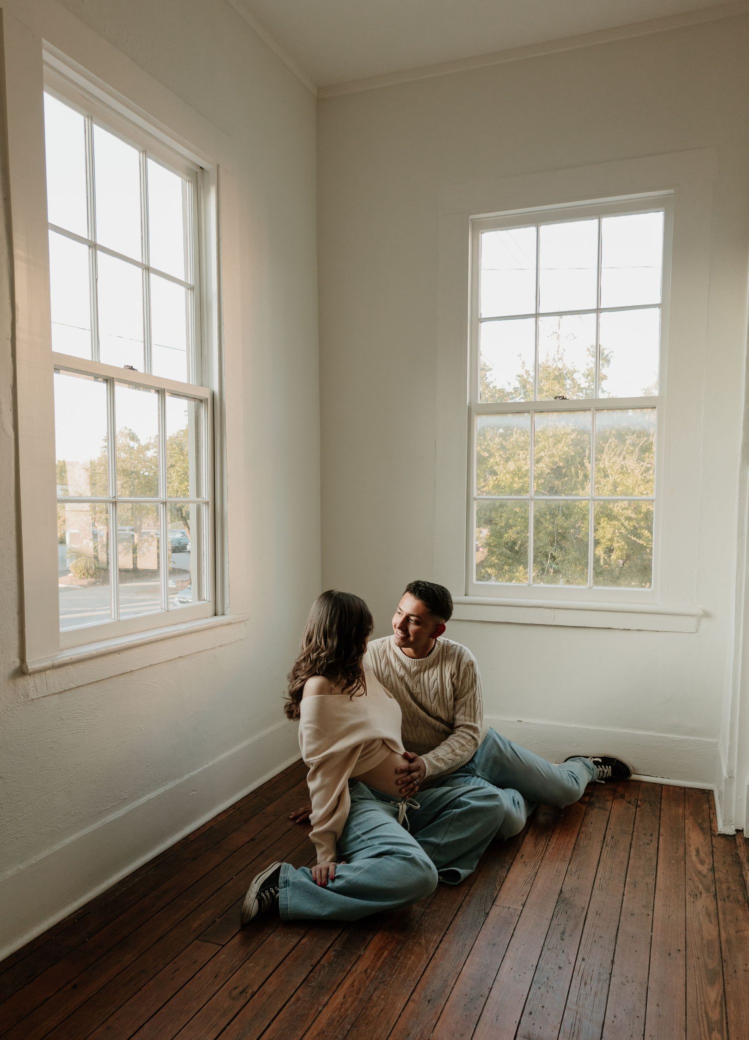 Couple relaxes together on wooden floor in minimalist white room with natural light.