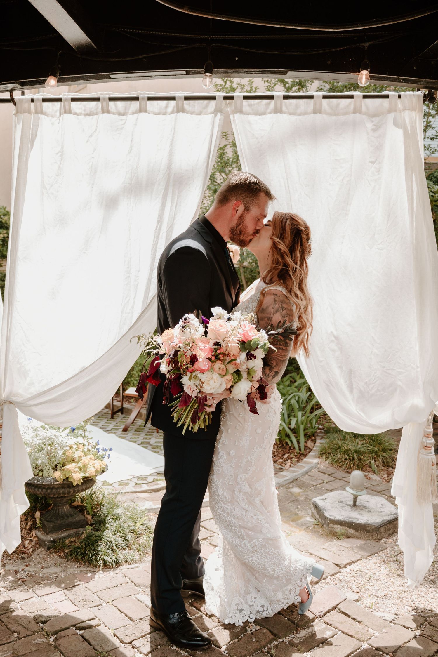 A couple shares their first kiss under flowing white curtains during an outdoor wedding ceremony.